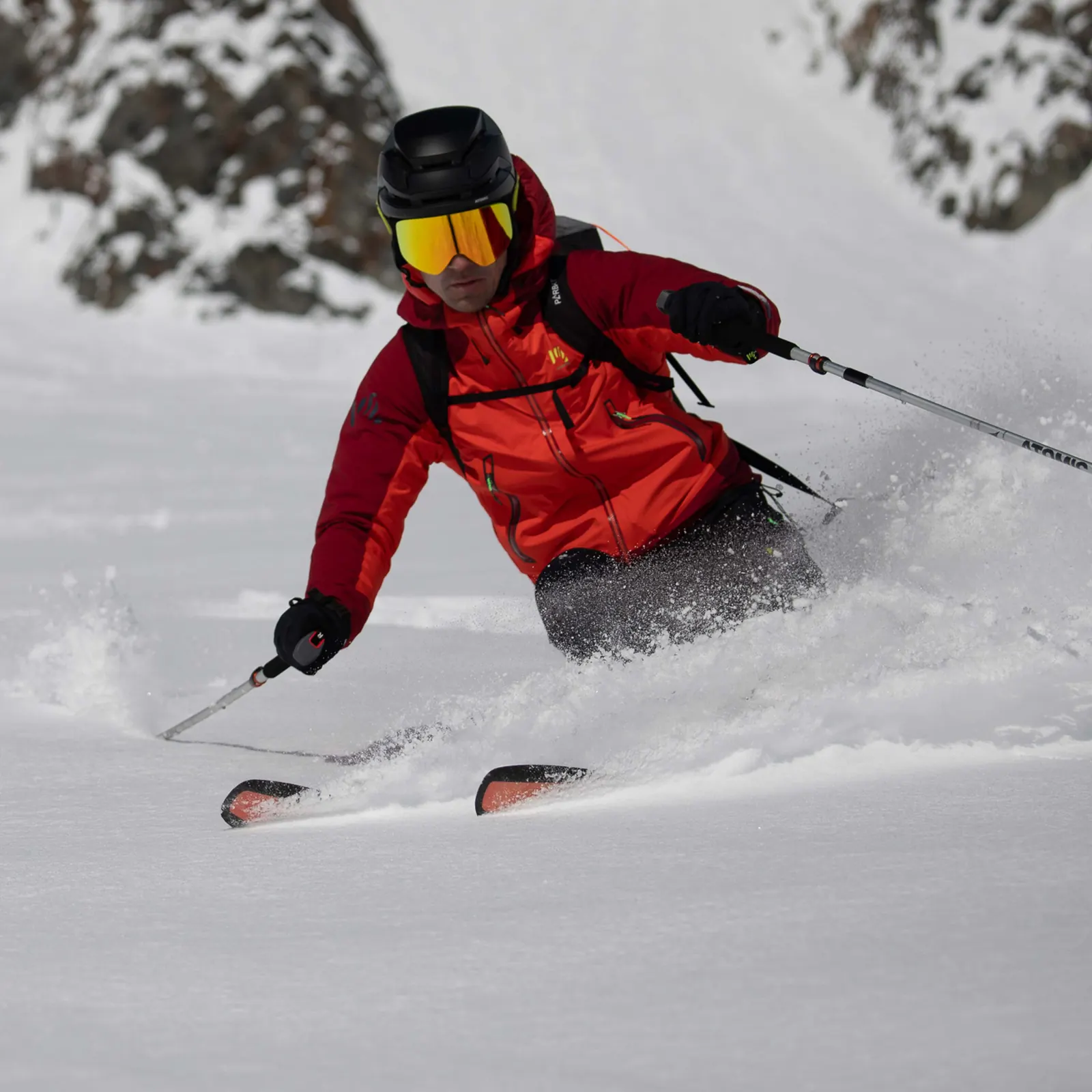 Skifahrer mit roter Jacke, Helm und Skibrille bei der Abfahrt durch tiefen Schnee