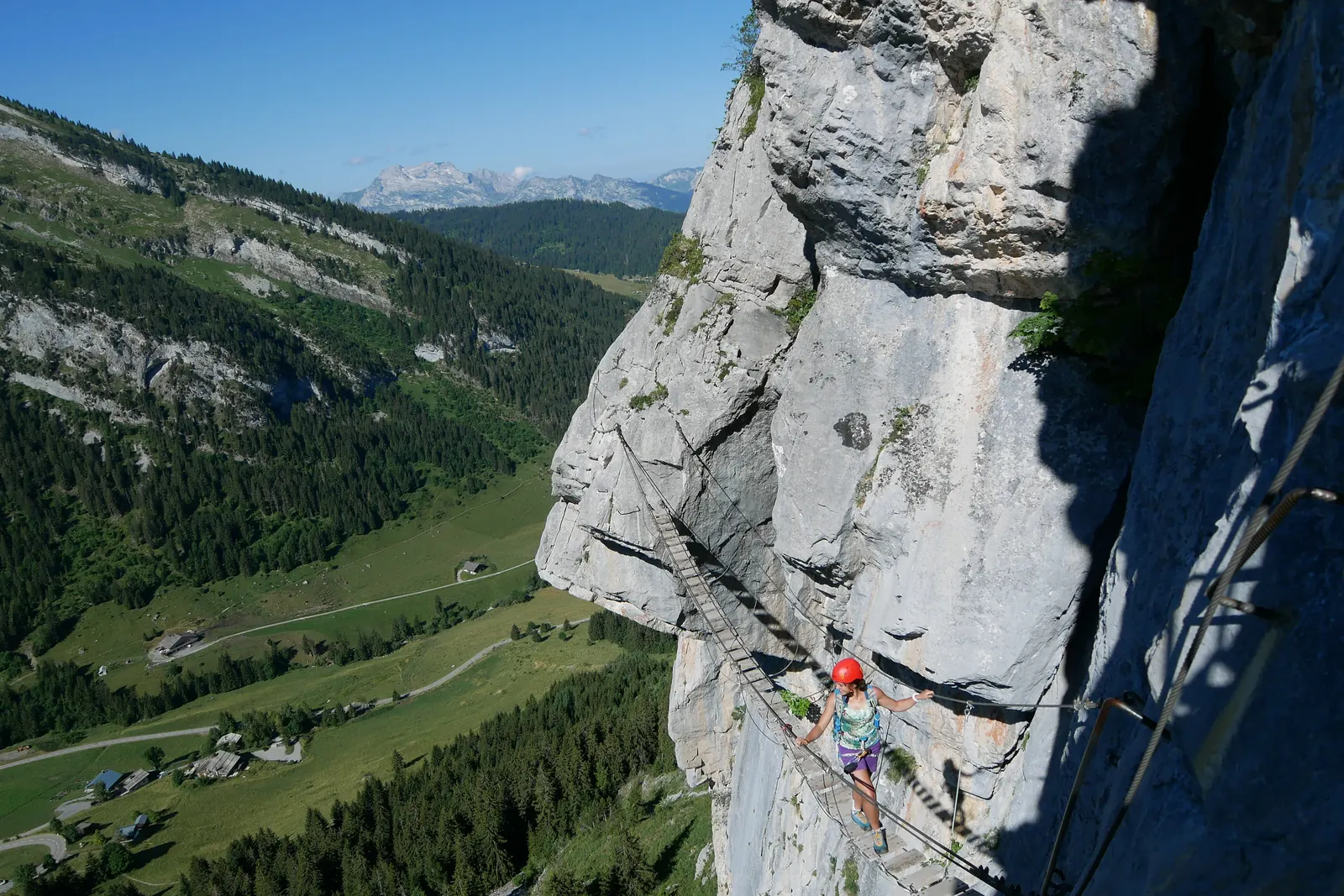 Kletternde Person mit rotem Helm in einer Felswand über einem grünen Tal