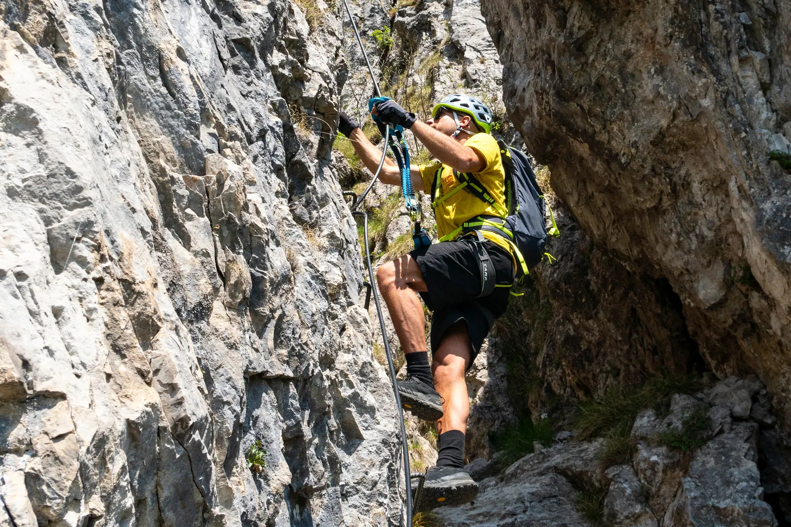 Person mit Helm und gelbem Oberteil an einer senkrechten Klettersteigpassage