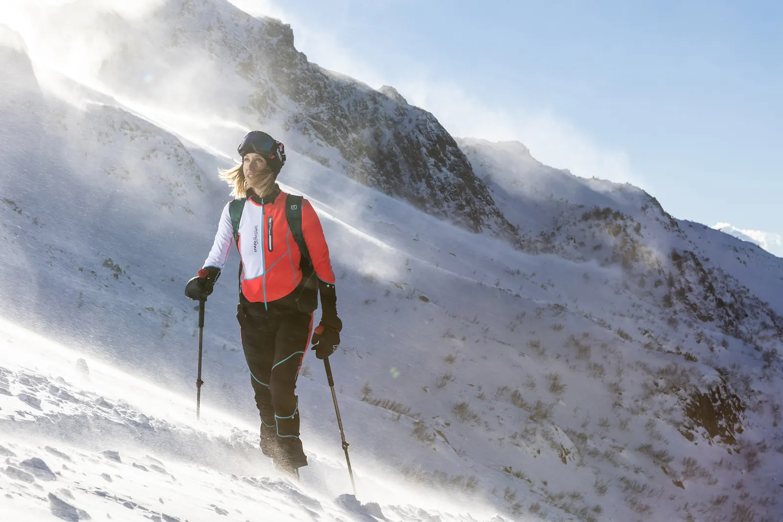 Sportlerin in rot-schwarzer Crazy-Bekleidung mit Rucksack und Stöcken im verschneiten Gebirge