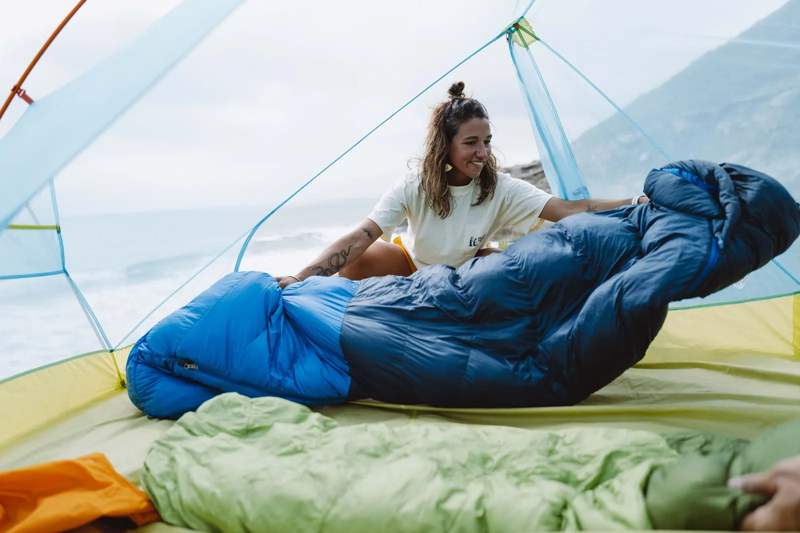 Eine Person breitet einen blauen Schlafsack in einem geöffneten Zelt aus