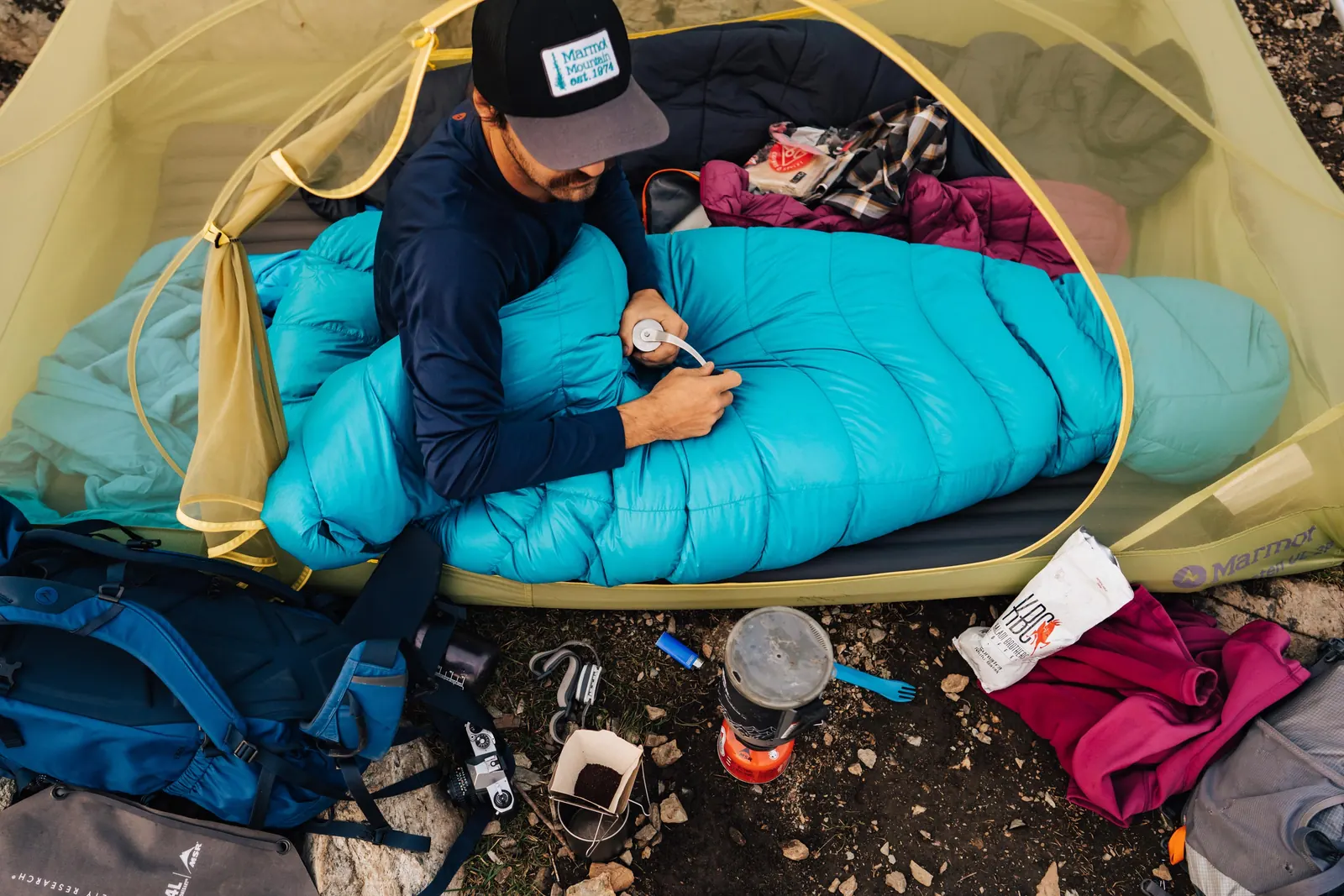 Person im türkisfarbenen Marmot-Schlafsack am geöffneten Zelteingang