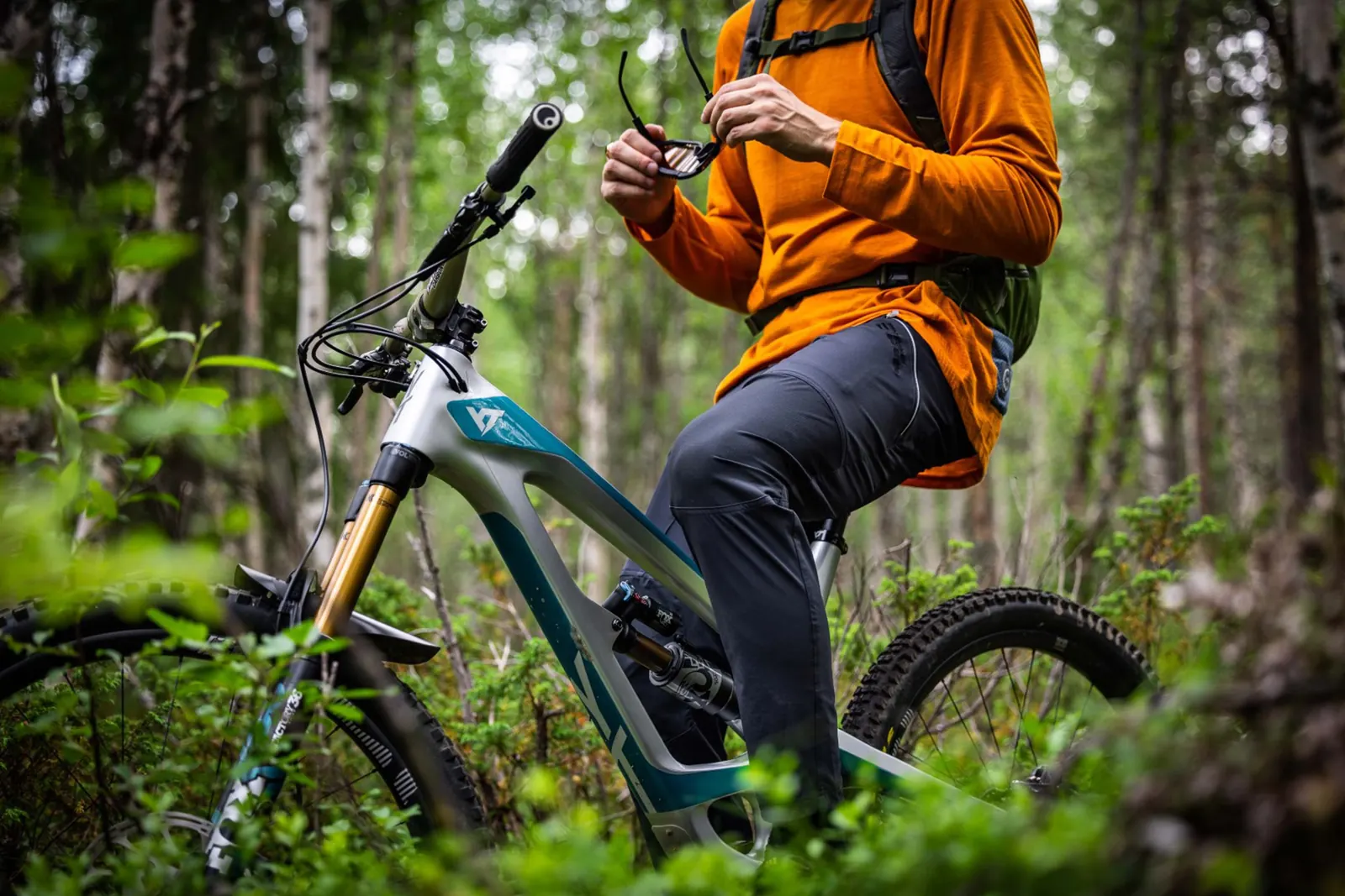 Person in orangefarbener Jacke mit einem Mountainbike auf einem Waldweg