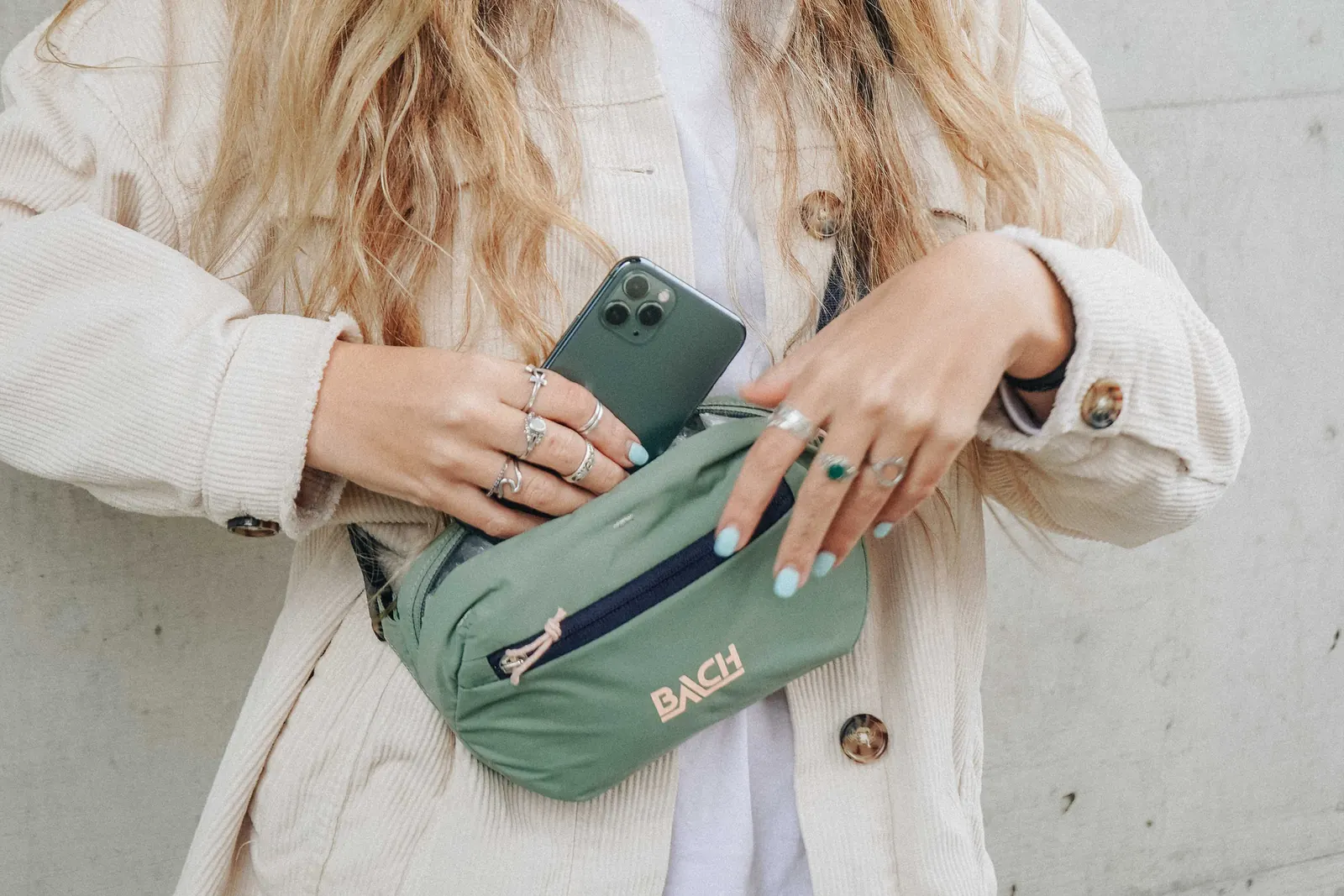 Person steckt ein Smartphone in eine quer getragene BACH Itsy Bitsy Bauchtasche