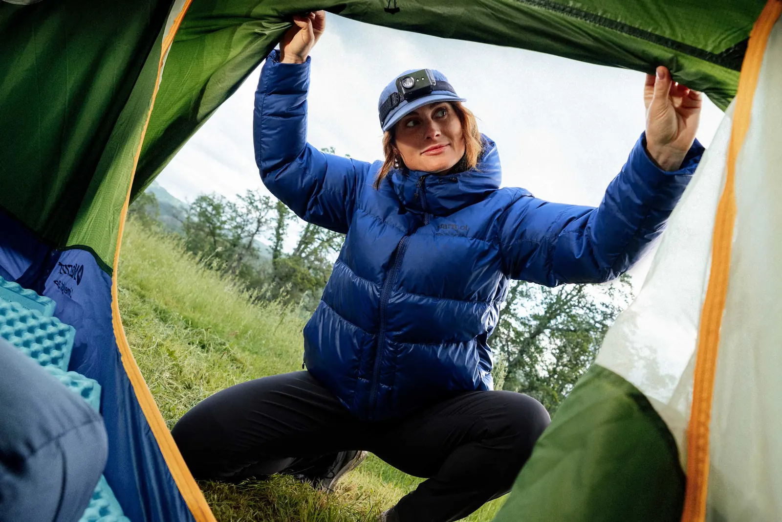 Person in blauer Daunenjacke mit Kapuze an einem Zelteingang