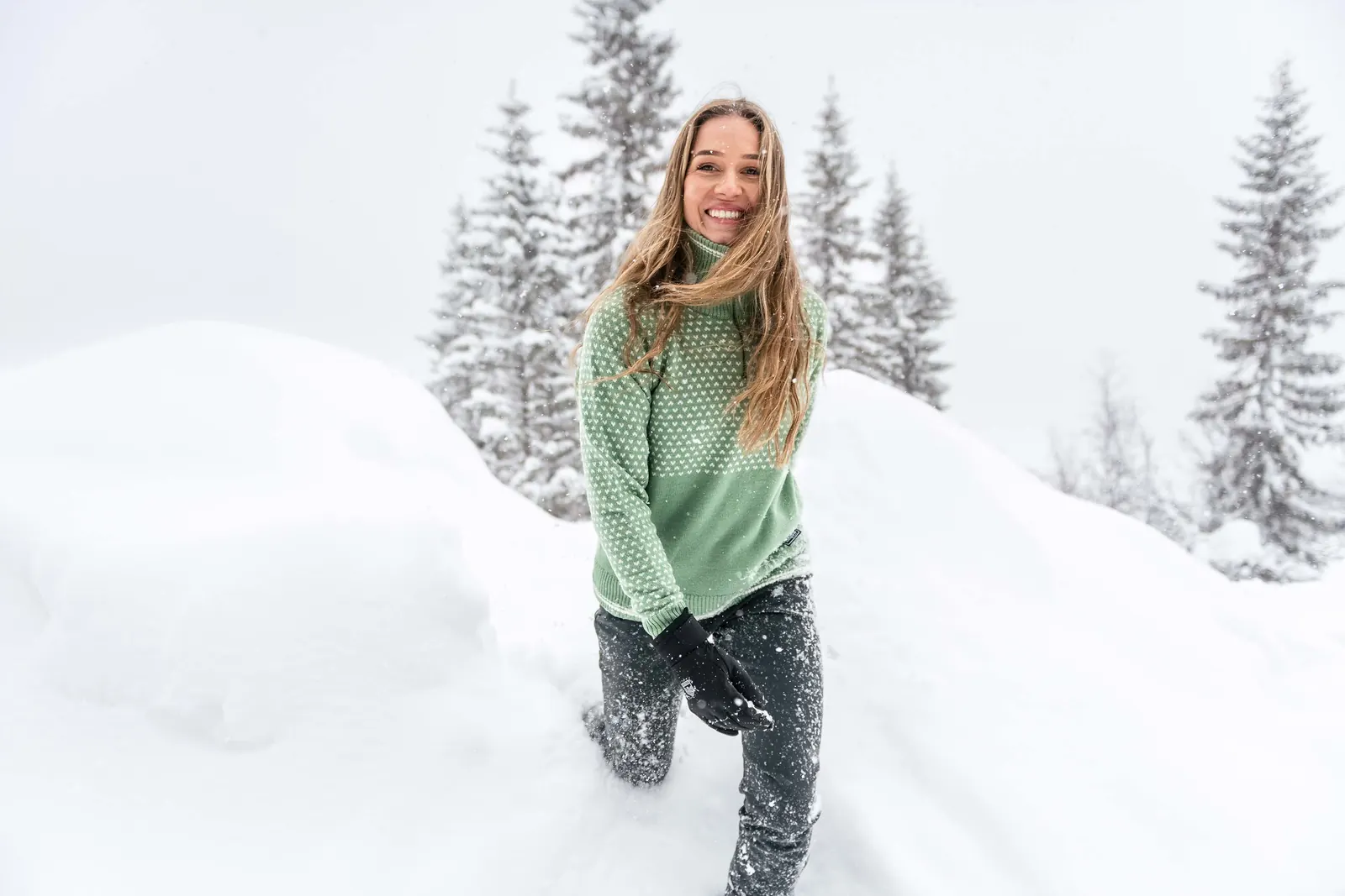 Frau in einem gemusterten Wollpullover zwischen verschneiten Bäumen