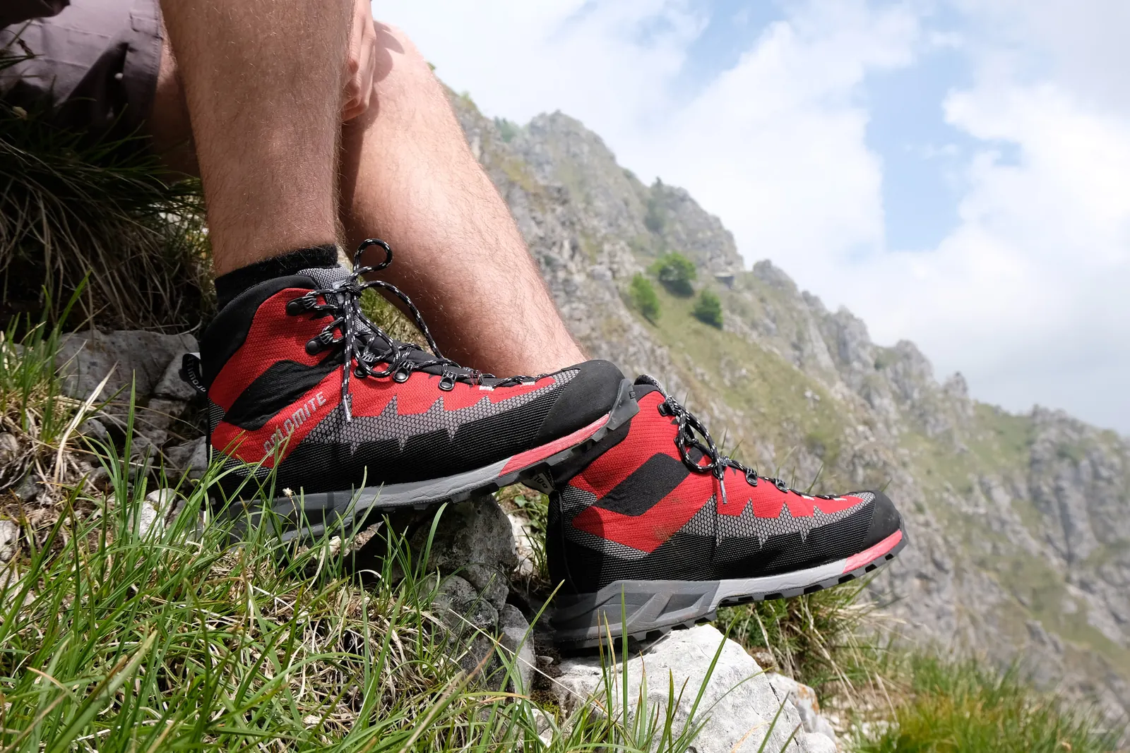 Rote Dolomite-Wanderschuhe an den Füßen einer Person auf einem grasigen Berghang