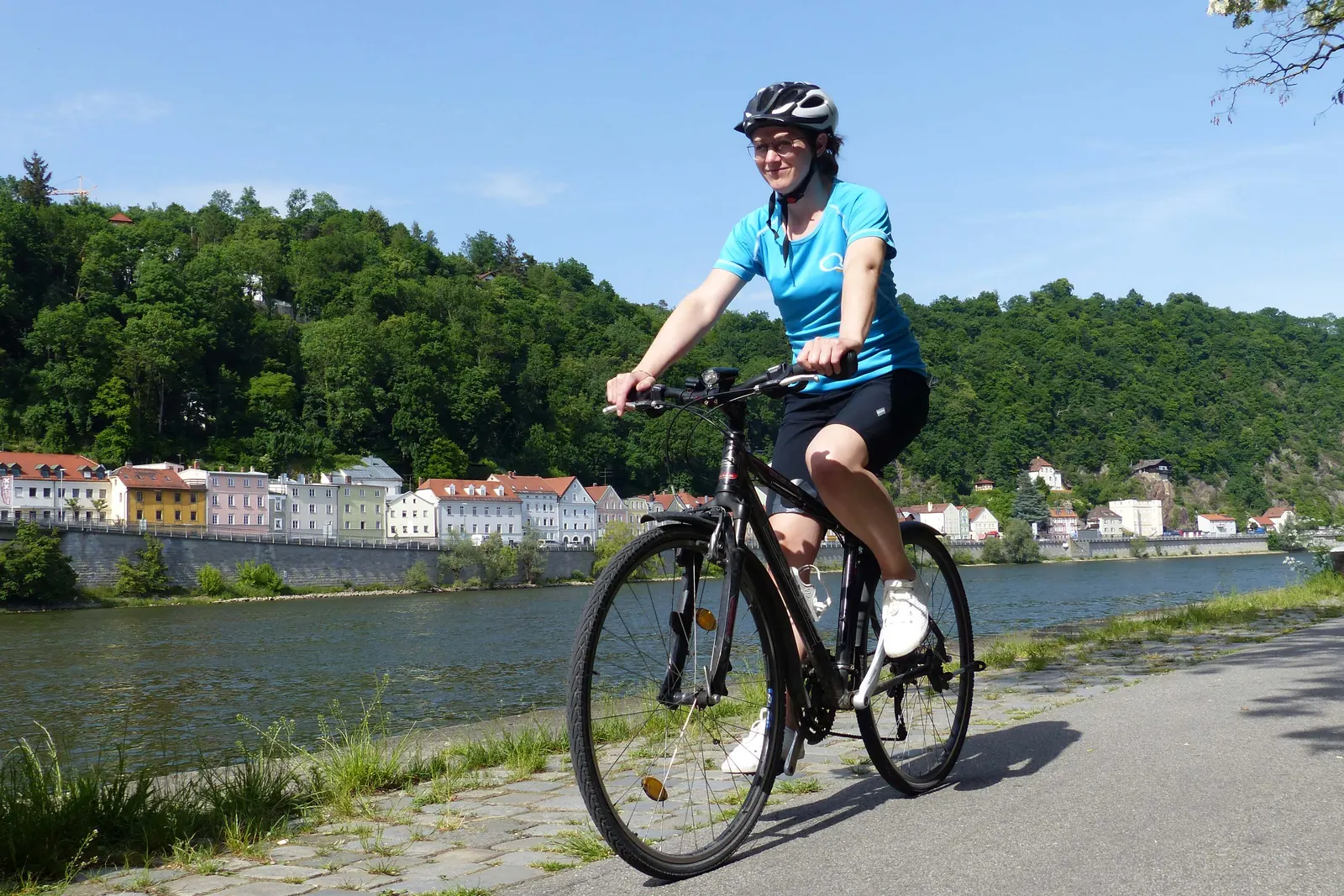 Radfahrerin mit türkisfarbenem Shirt und schwarzer Shorts auf einem Weg am Fluss