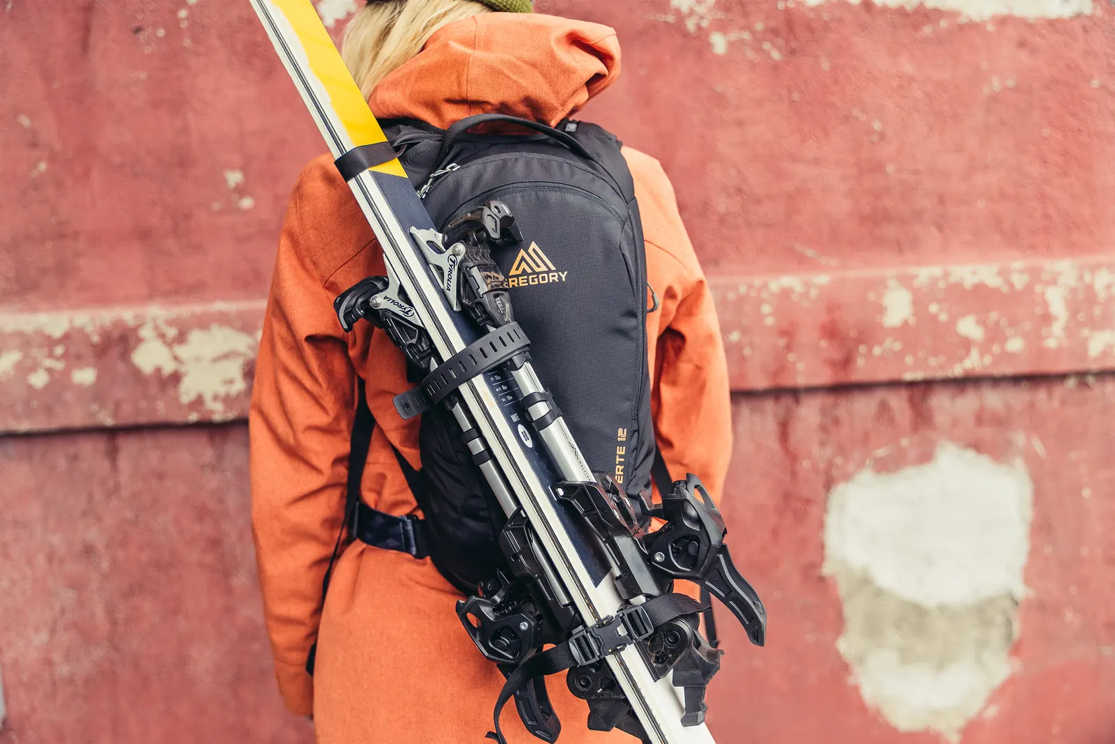 Person mit diagonal am schwarzen Gregory-Rucksack befestigten Skiern