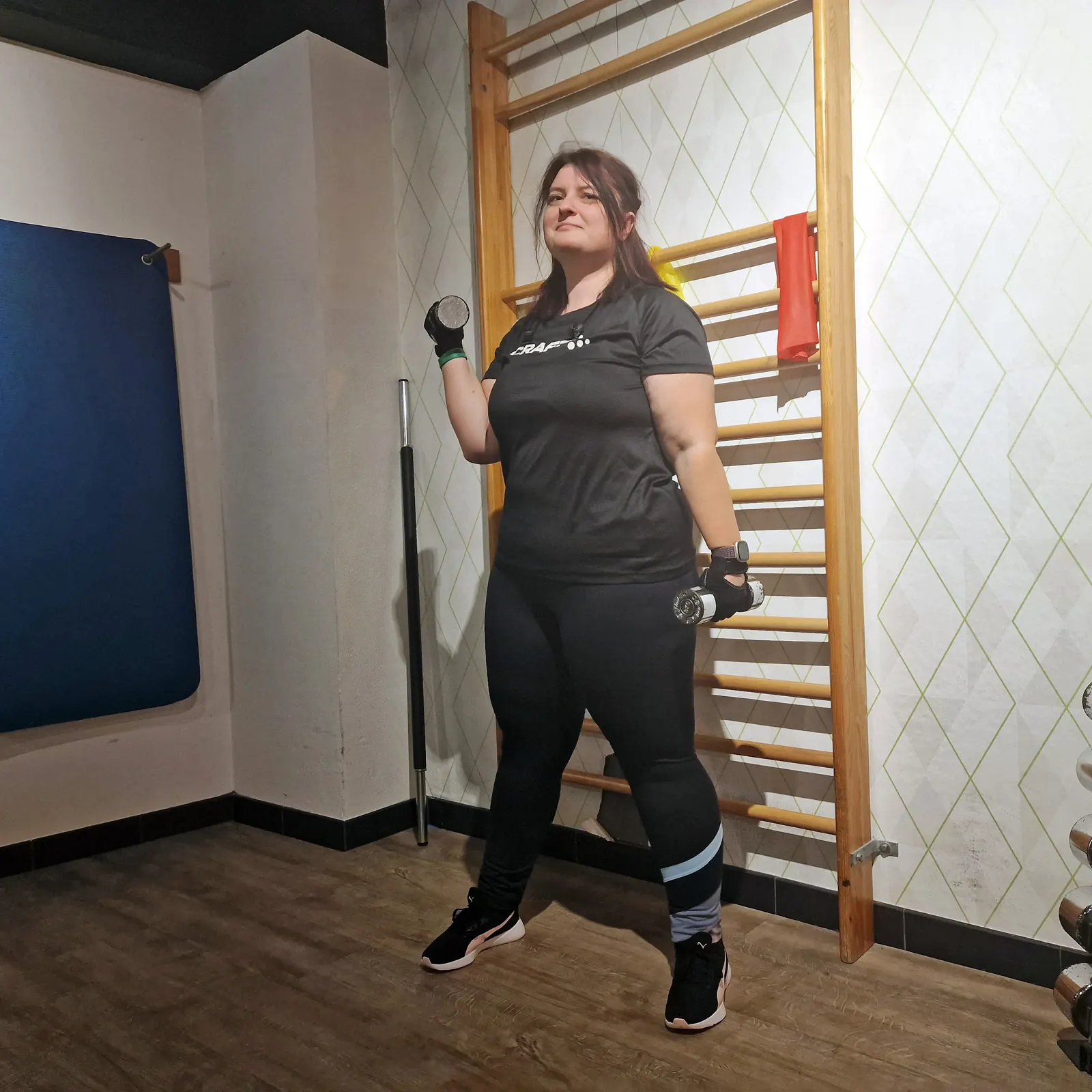 Sportlerin mit Kurzhanteln im schwarzen Craft-Shirt und gemusterten CMP-Leggings