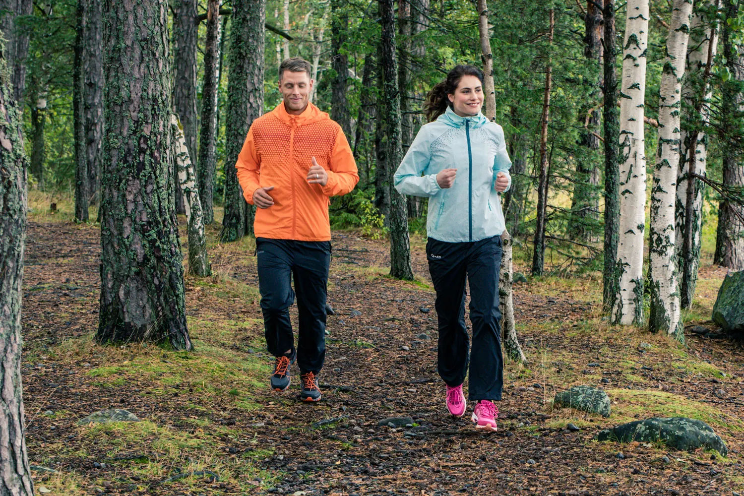 Zwei Personen in orangefarbener und hellblauer Laufjacke auf einem Waldweg