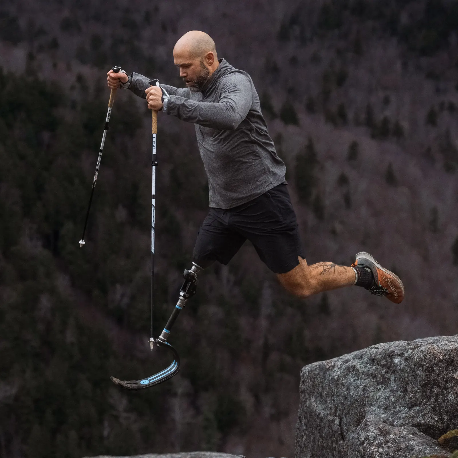 Sportler mit Beinprothese und zwei Stöcken springt über einen Felsblock