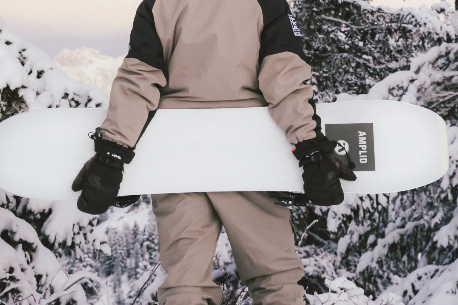 Snowboarder hält ein weißes Snowboard mit schwarzen LEVEL-Fäustlingen im Schnee