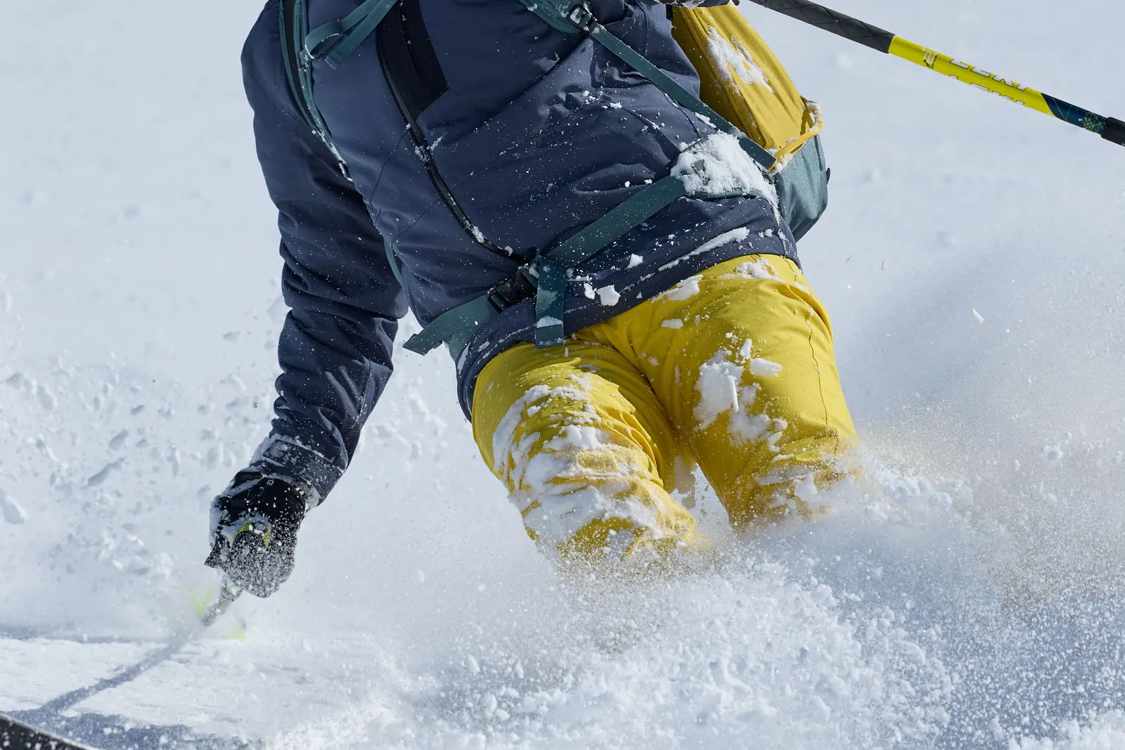 Gelbe Maier-Sports-Skihose bei einer Abfahrt durch aufgewirbelten Schnee