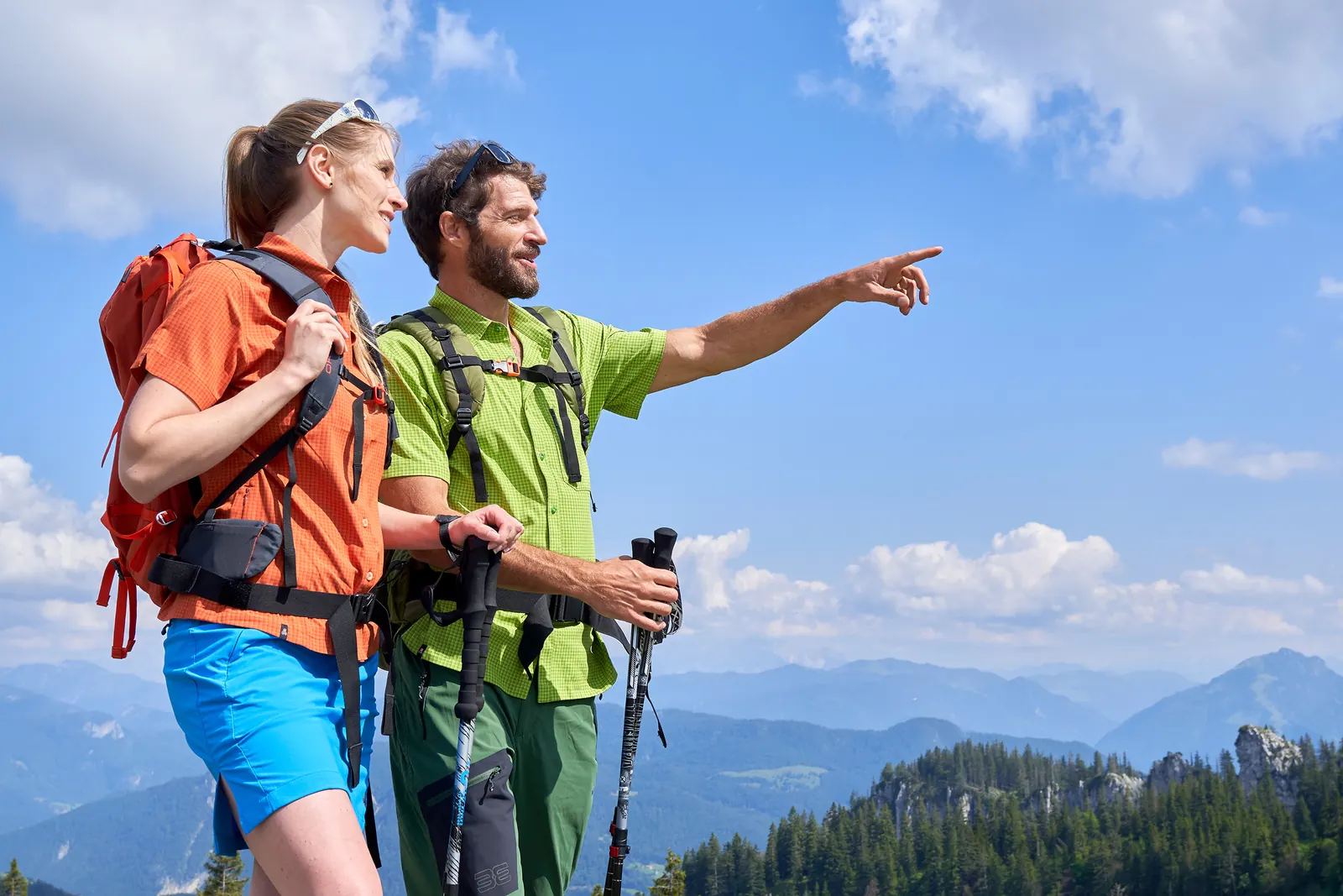 Zwei Wanderer mit Rucksäcken und Stöcken vor einem Bergpanorama