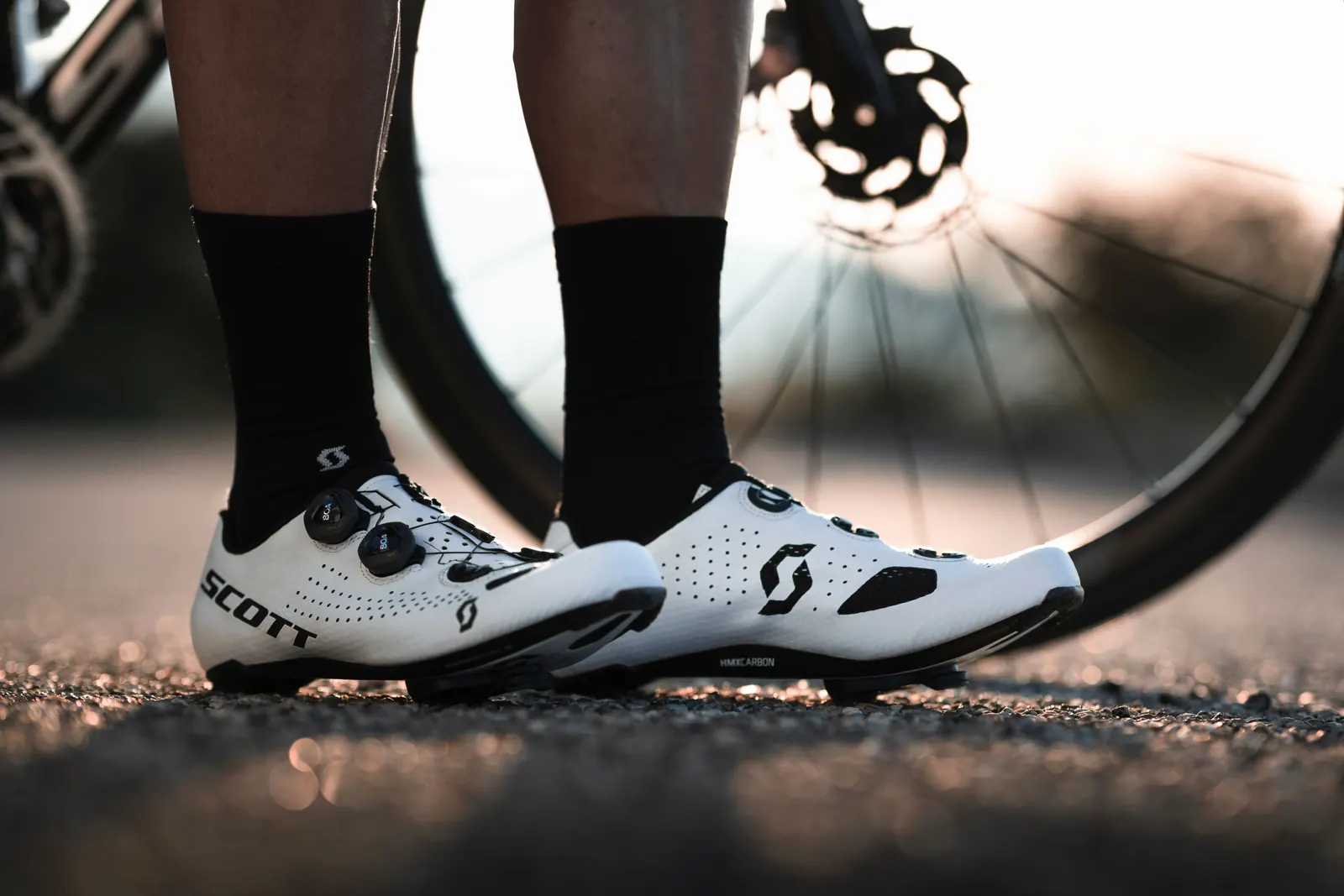 Weiße Scott-Rennradschuhe mit Drehverschluss und Zusatzriemen neben einem Rennrad