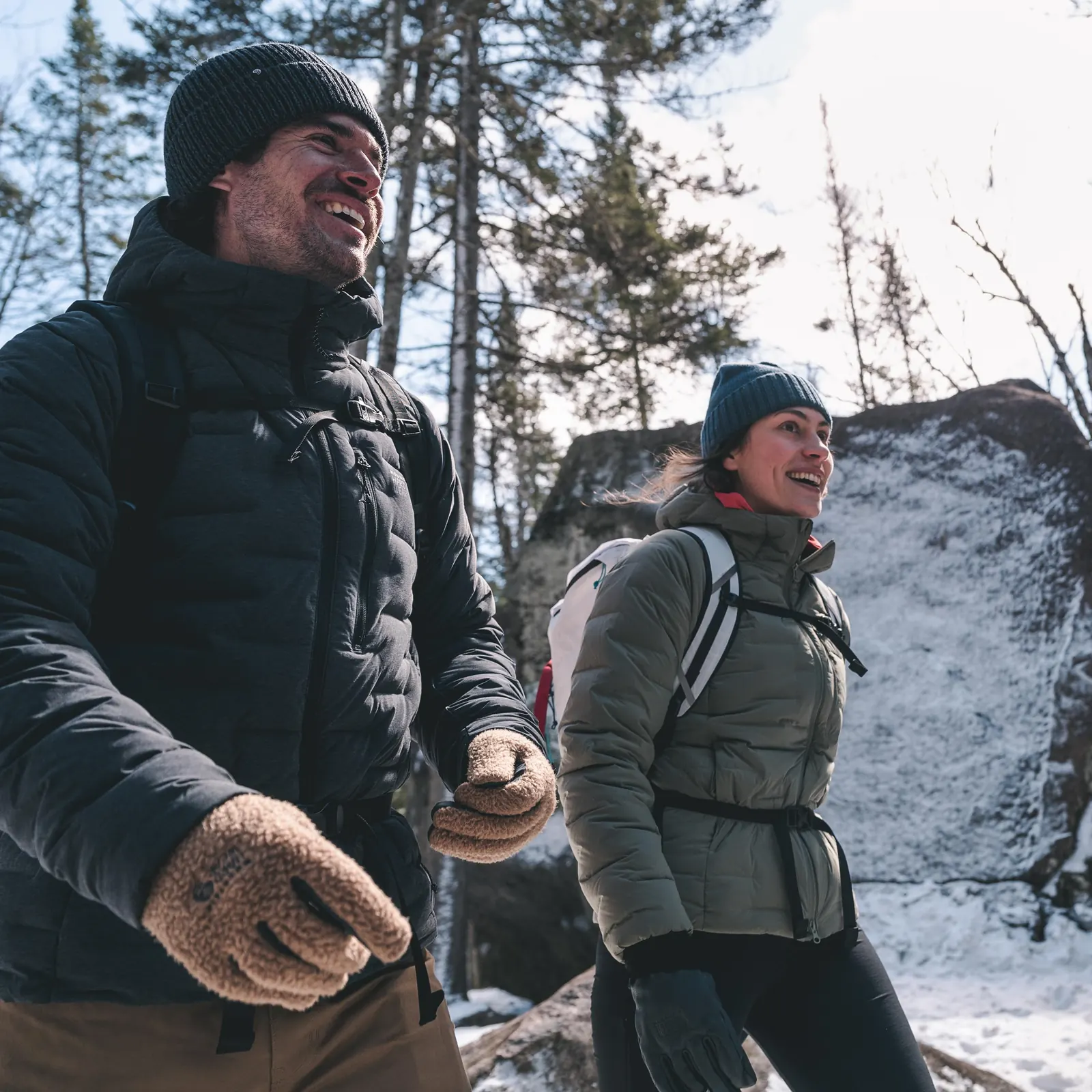 Zwei Personen mit Daunenjacken und Rucksäcken auf einem verschneiten Waldweg