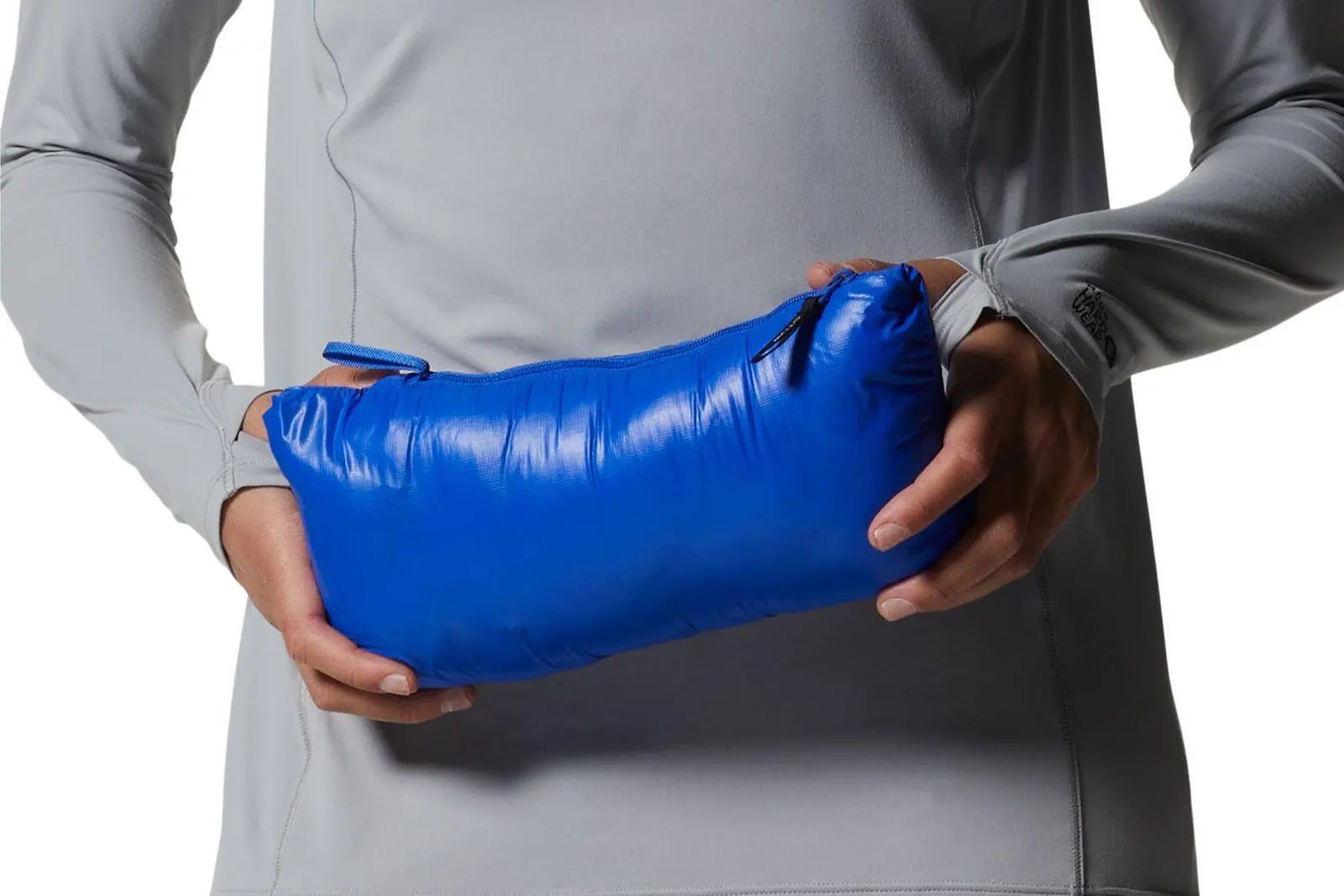 Person hält eine kompakt verstaute blaue Daunenjacke vor dem Körper