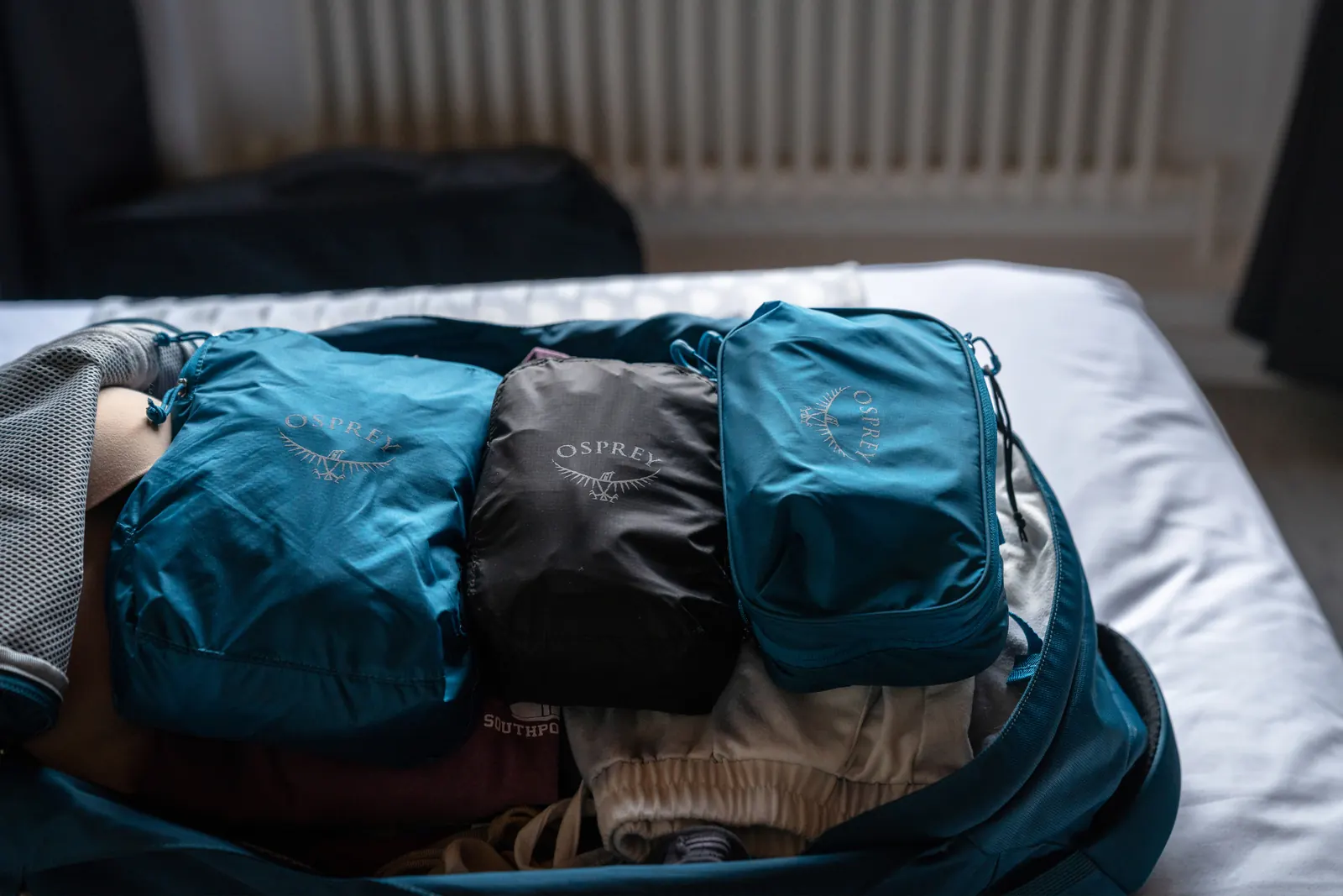 Offener Trekkingrucksack mit mehreren Packbeuteln auf einem Bett