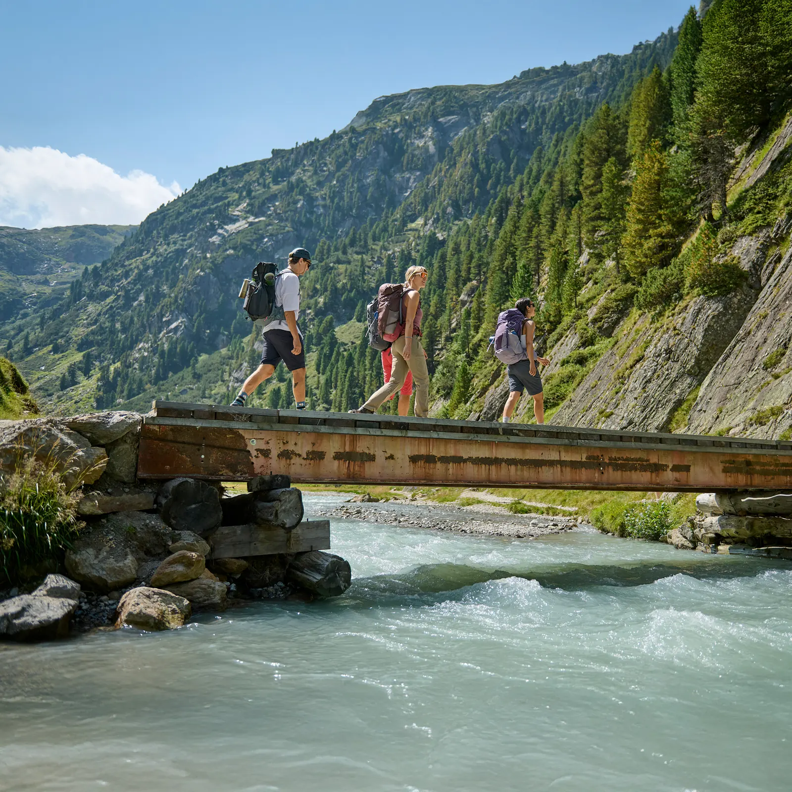 Wanderin in langer Outdoorhose mit aufspritzendem Wasser am Ufer eines Bergsees