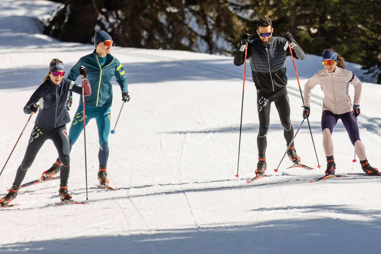 Vier Langläufer in körpernaher Winterbekleidung auf einer sonnigen Loipe