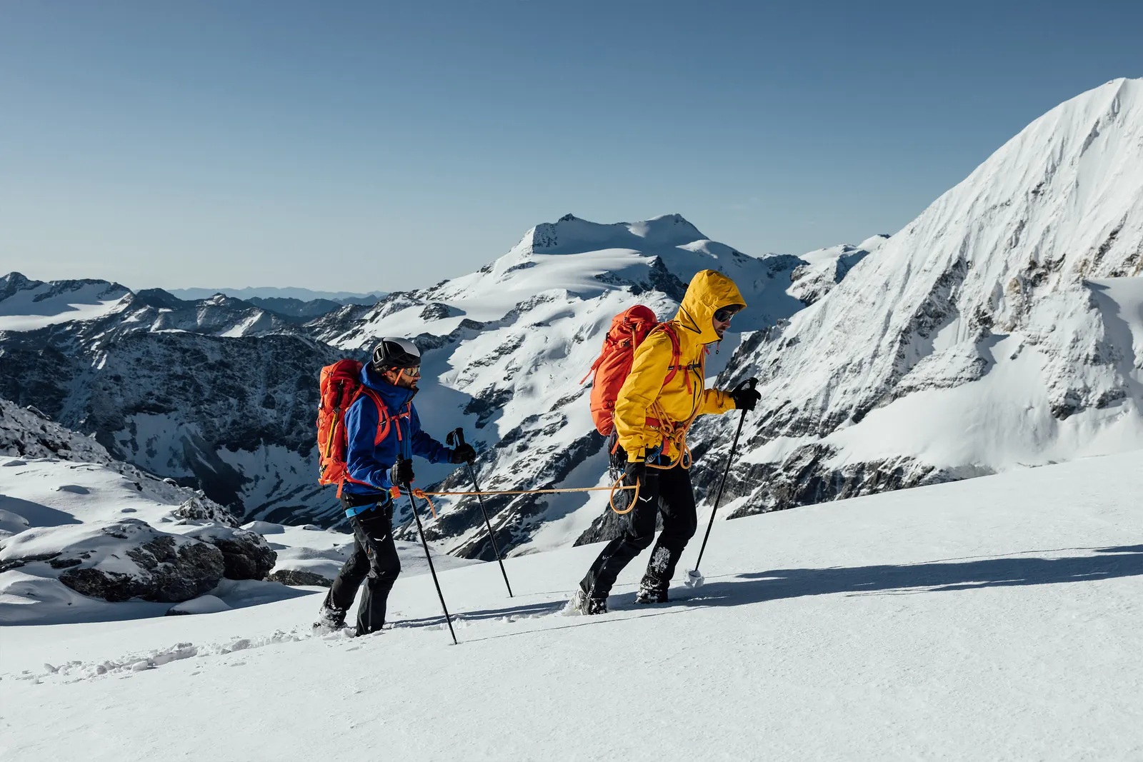 Zwei Bergsteiger mit Rucksäcken beim Aufstieg über einen verschneiten Hang