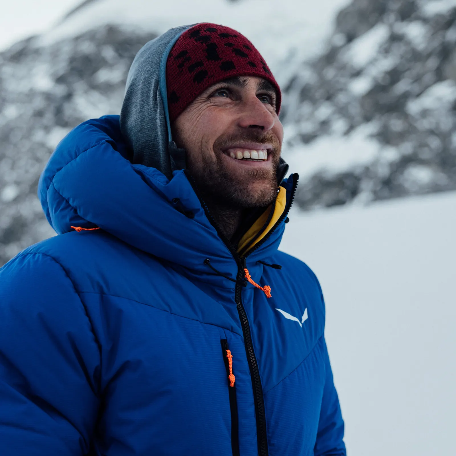 Gabriel Tschurtschenthaler in einer blauen Isolationsjacke vor verschneiten Bergen