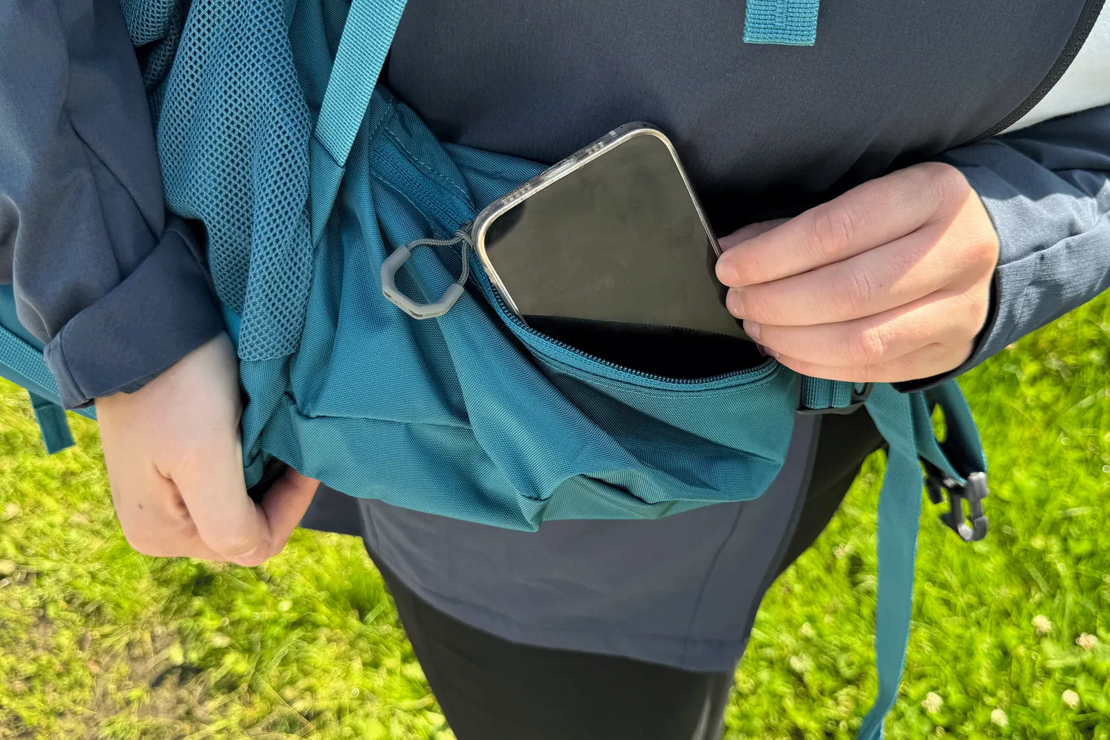 Ein Smartphone wird in die geöffnete Hüftgurttasche des Gregory Amber 68 gesteckt