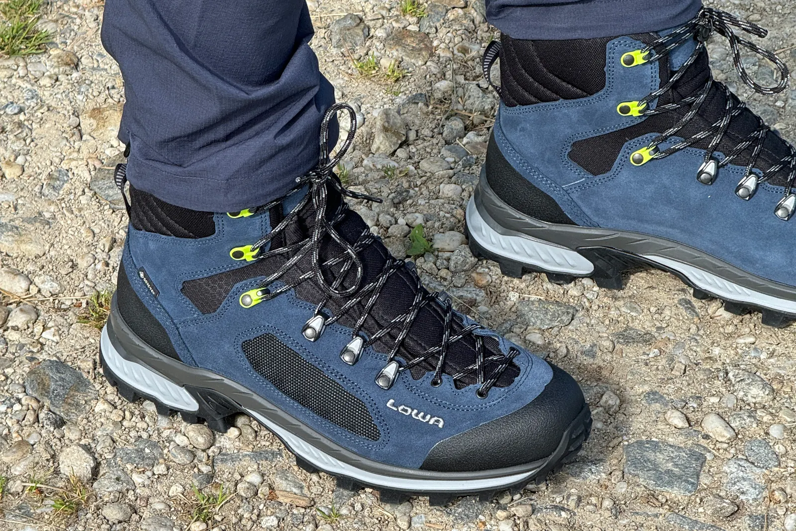 Blauer LOWA Corvara GTX Mid mit Textileinsätzen und schwarzer Zehenkappe auf steinigem Weg