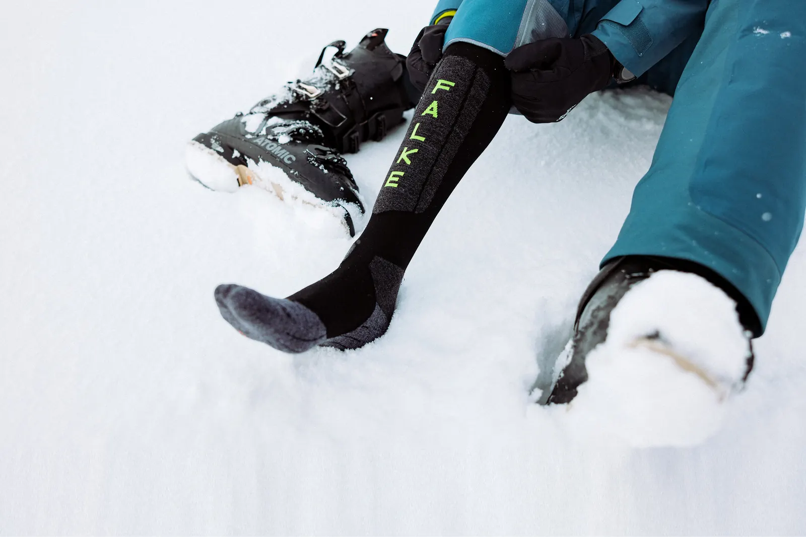 FALKE-Skistrumpf am Fuß neben geöffneten Skischuhen im Schnee