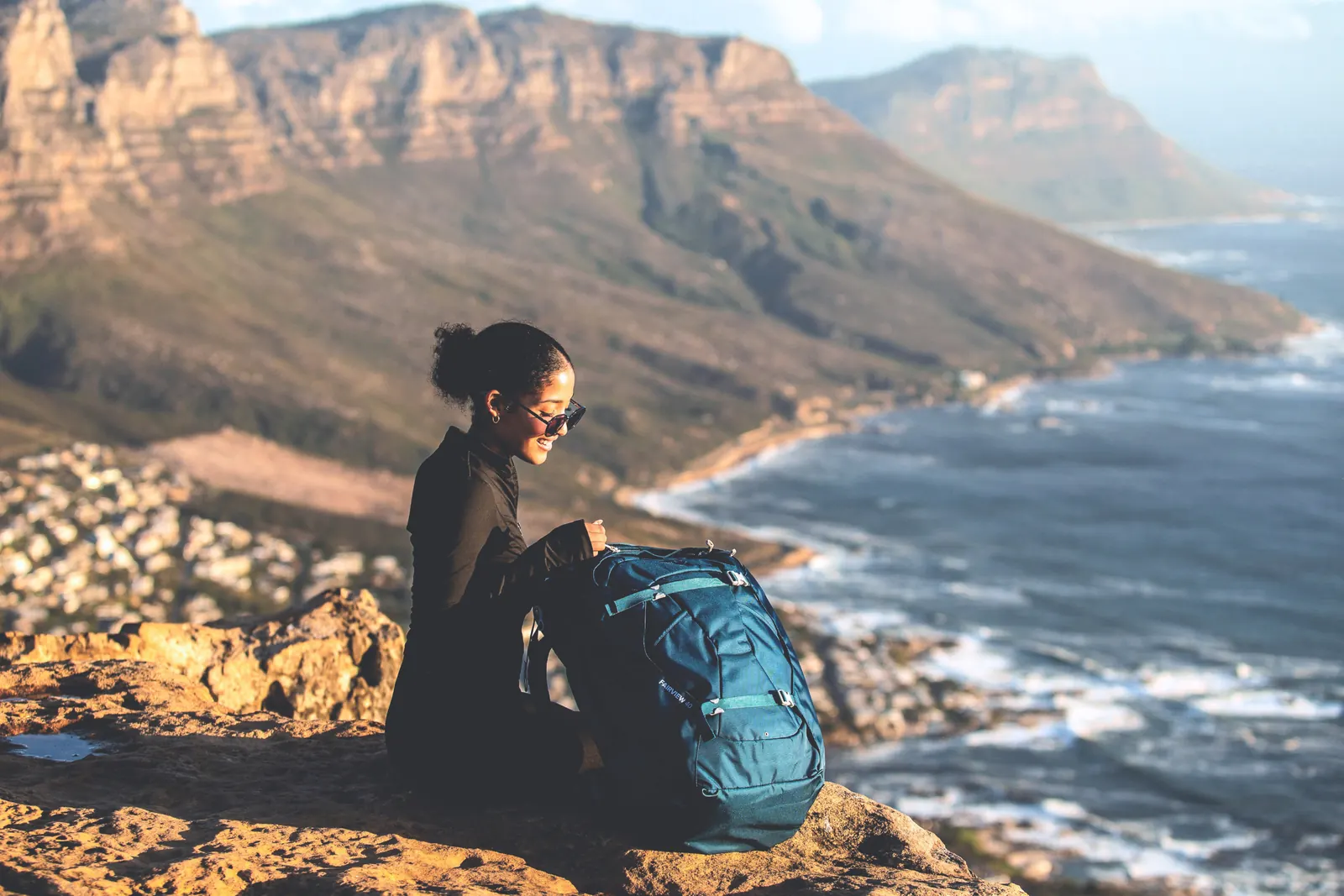 Wanderin mit einem blauen Rucksack auf einem Felsen oberhalb der Küste
