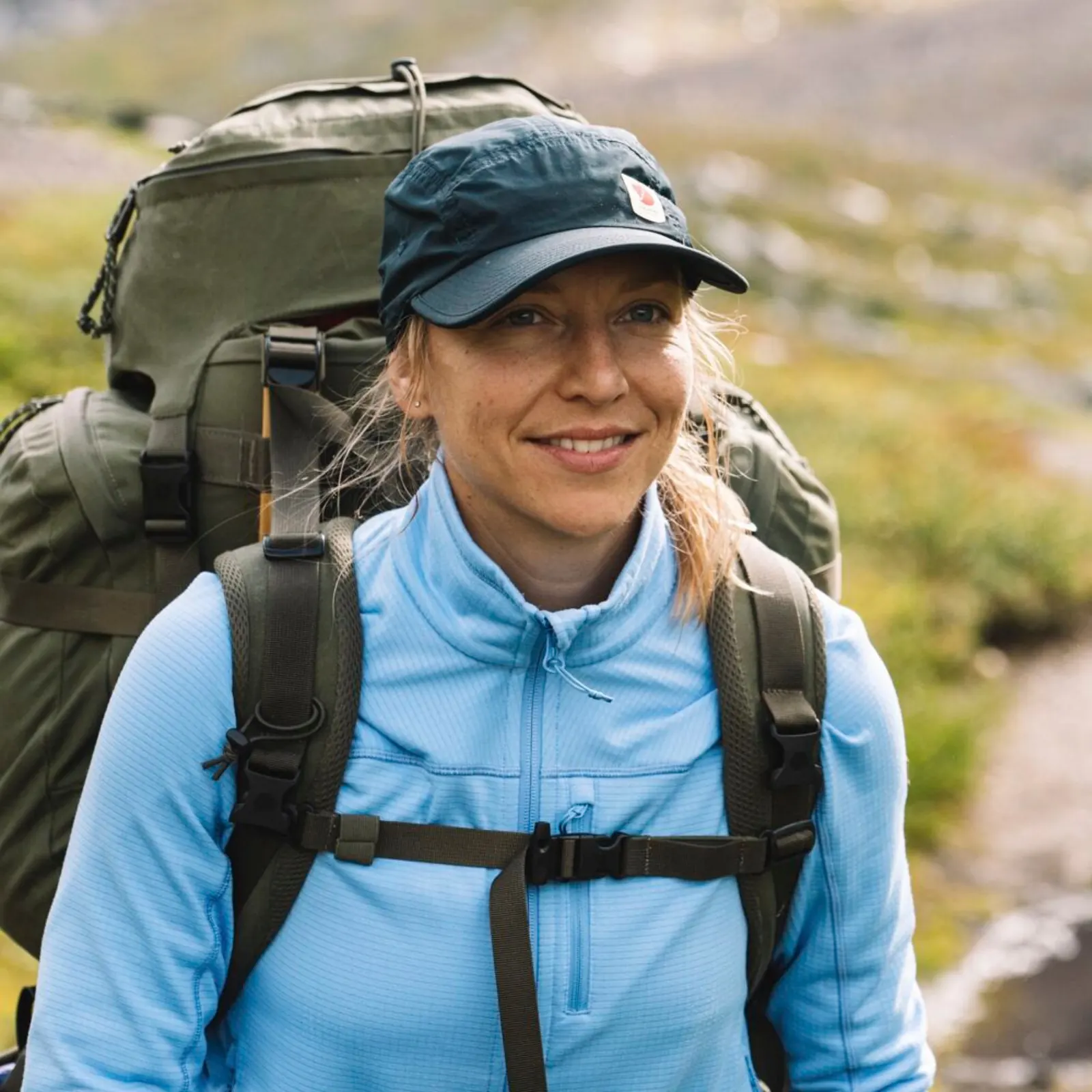 Wanderin mit Fjällräven-Kappe, blauem Oberteil und großem Trekkingrucksack
