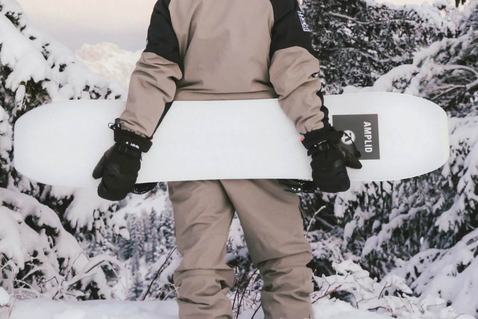 Person mit schwarzen Handschuhen hält ein weißes Snowboard im verschneiten Wald