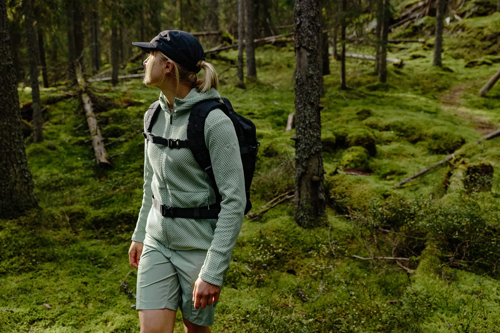 Wanderin mit Kappe, Rucksack, leichter Jacke und Shorts auf einem Waldweg
