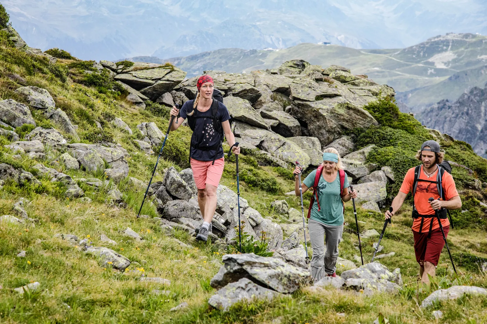 Drei Personen steigen mit Wanderstöcken einen steinigen Bergpfad hinauf