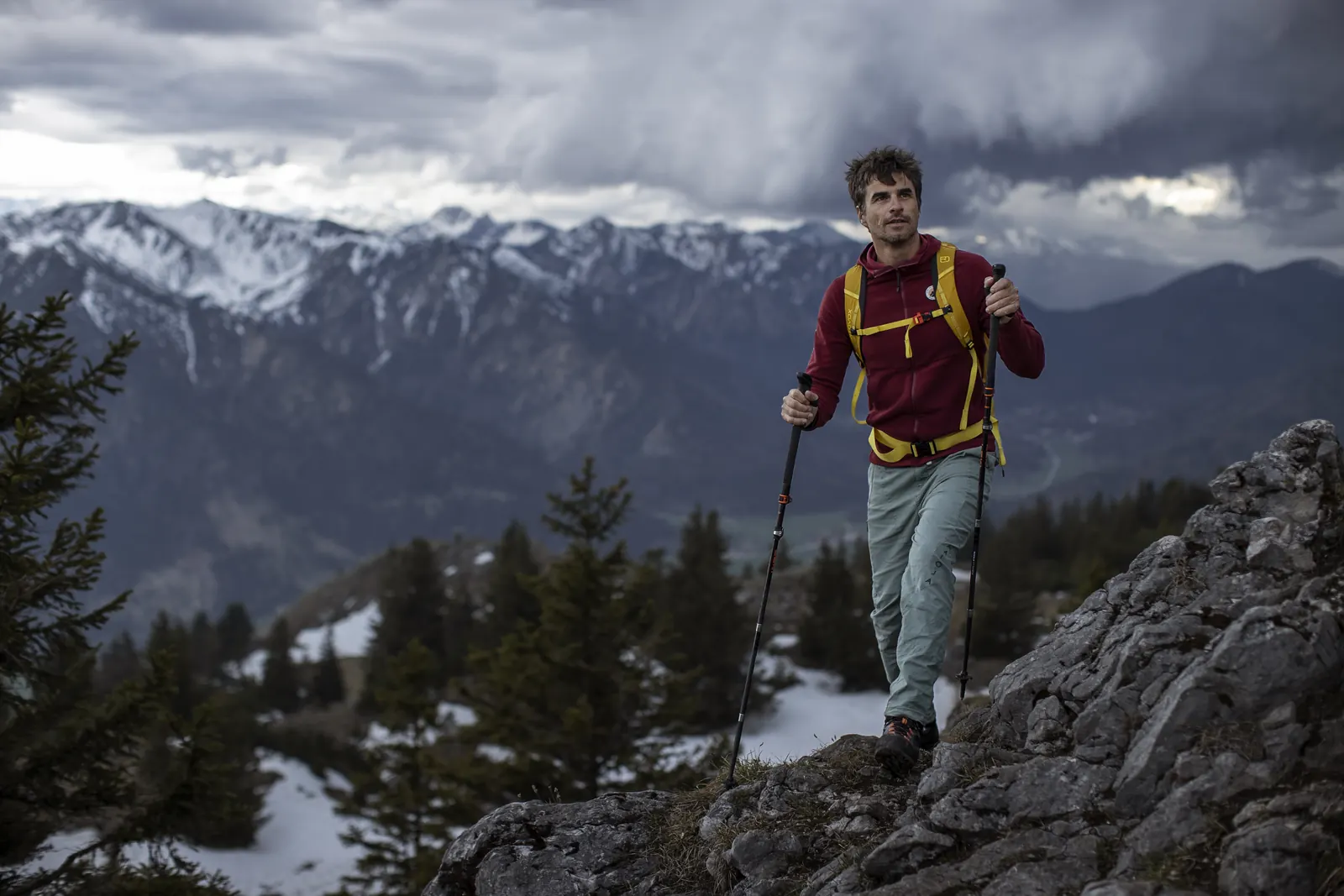 Eine Person geht mit zwei Wanderstöcken auf einem schmalen felsigen Bergpfad