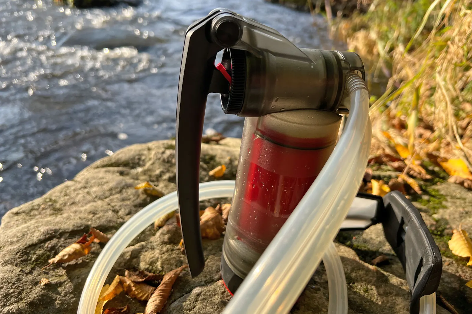 MSR Guardian mit Pumphebel und aufgewickeltem Doppelschlauch am Flussufer