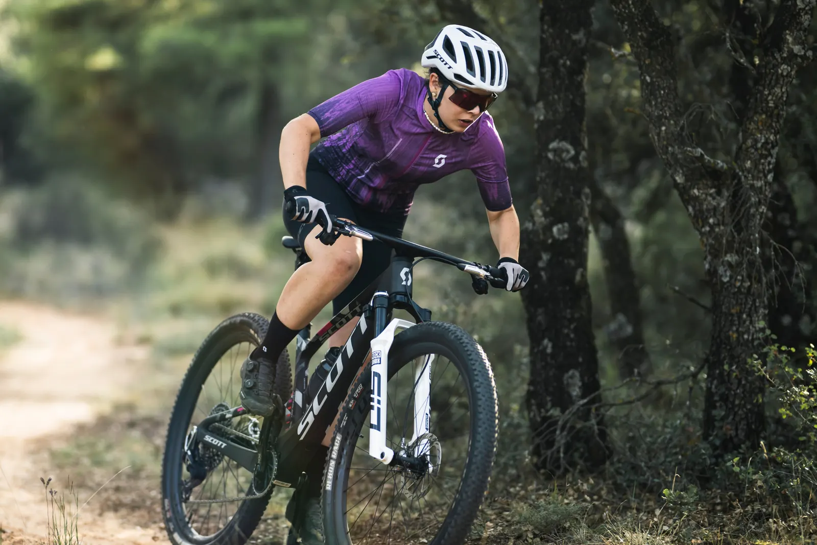 Eine Person im violetten Kurzarmtrikot fährt mit einem Mountainbike durch eine Waldkurve