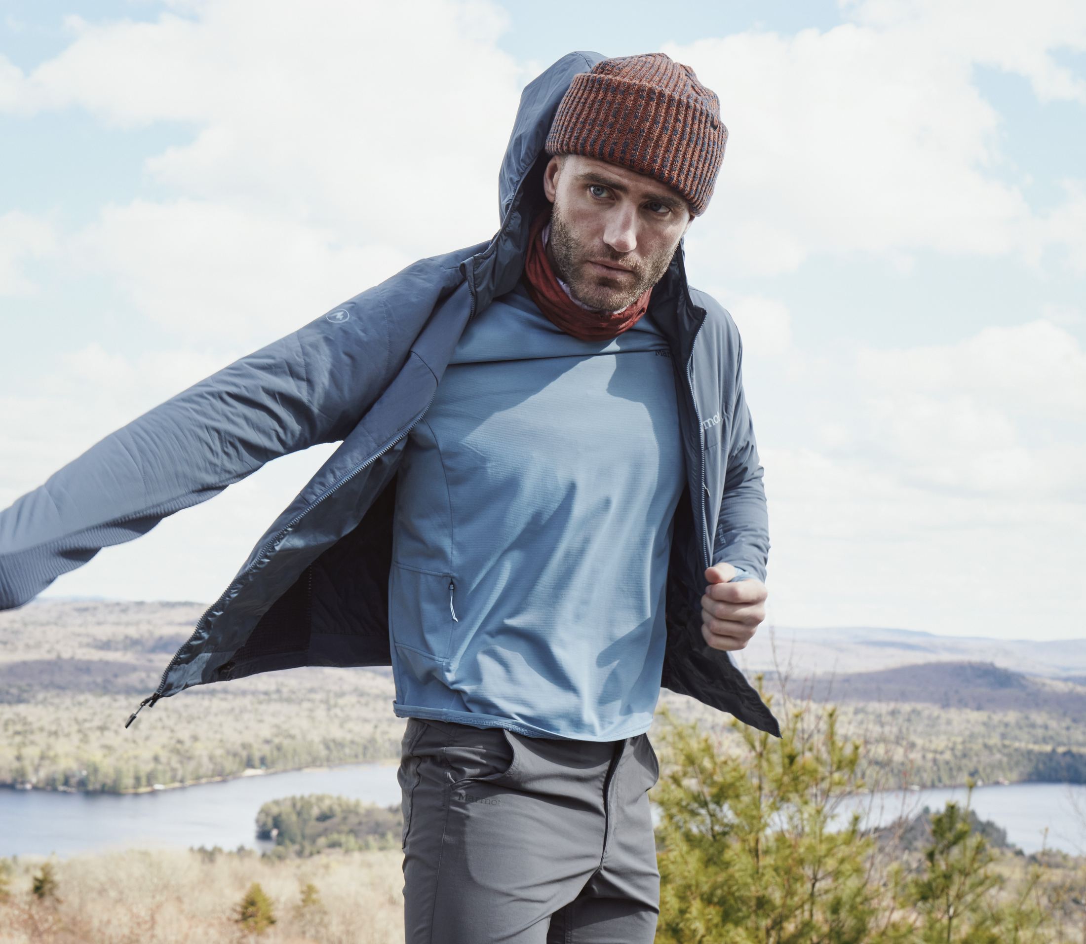 Wanderer mit Rucksack in der Marmot Revlo Hybrid Hoody, Gesicht sichtbar, in Bewegung am Berg