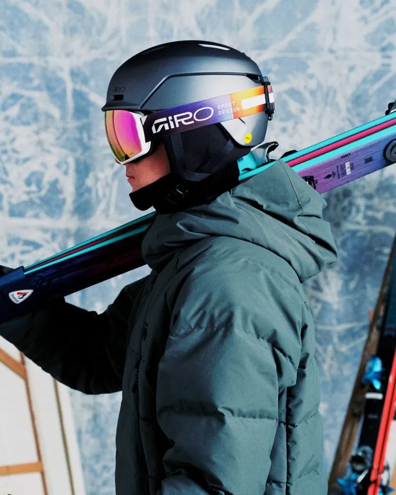 Female skier with a dark Giro Neo Mips II and Giro ski goggles, skis over her shoulder