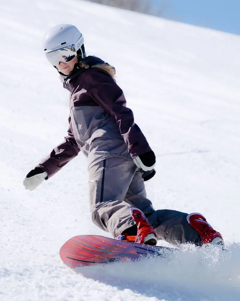 Female snowboarder wearing a Giro Neo Mips II in Lavender, making a turn on the piste