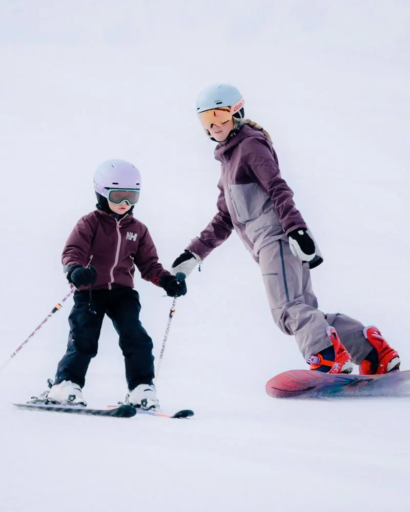 Child skiing and female snowboarder wearing Giro helmets on the piste