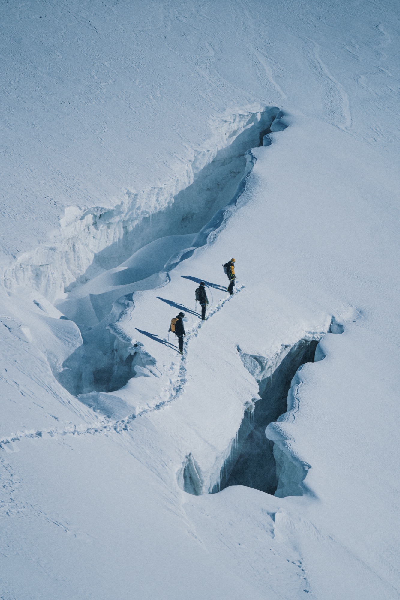 Drei Alpinisten überqueren an einem Seil eine Gletscherspalte im Hochgebirge