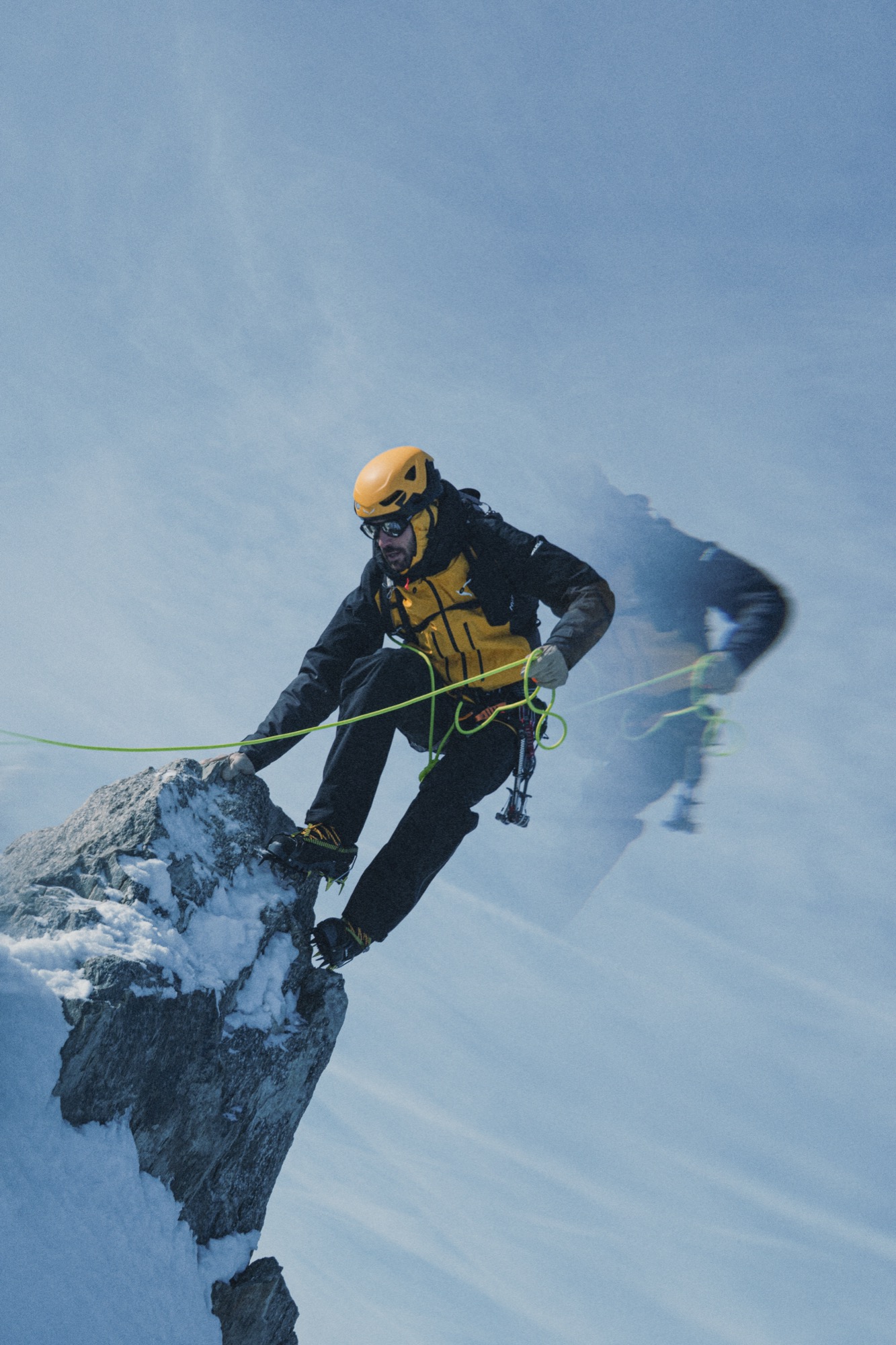 Ein Alpinist klettert gesichert über einen schneebedeckten Felsgrat