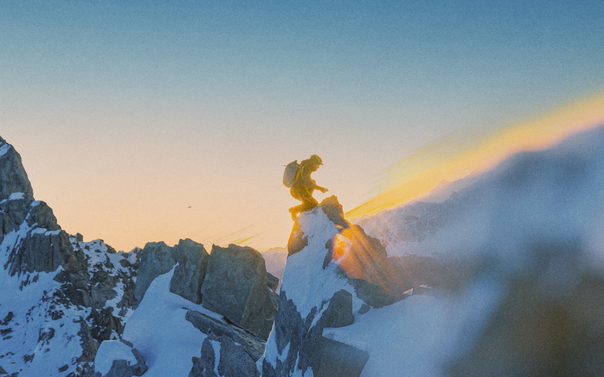Ein Alpinist im Gegenlicht auf einem schneebedeckten Felsgrat bei Sonnenuntergang