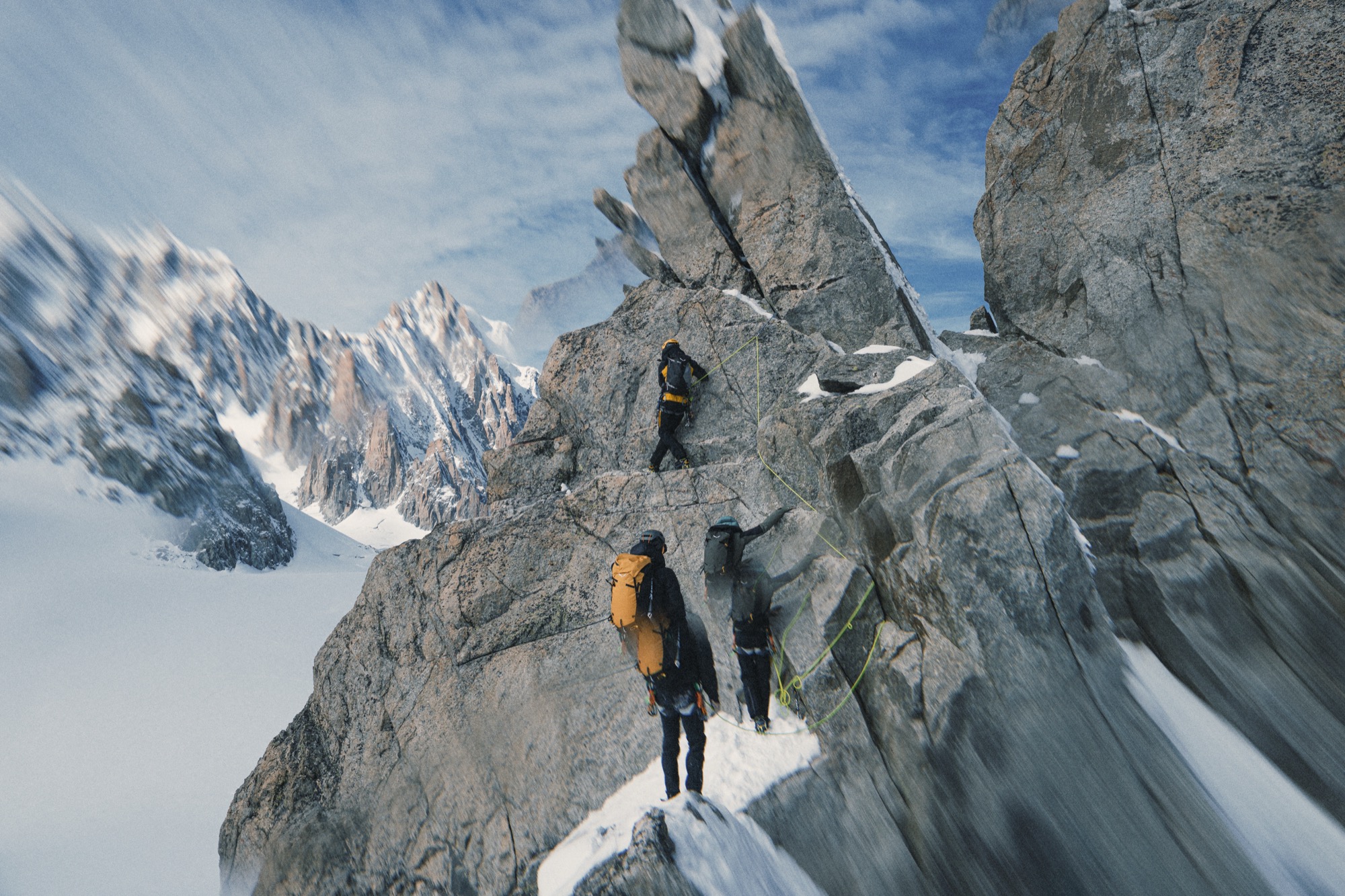 Zwei Alpinisten mit gelben Rucksäcken steigen über einen Felsgrat auf