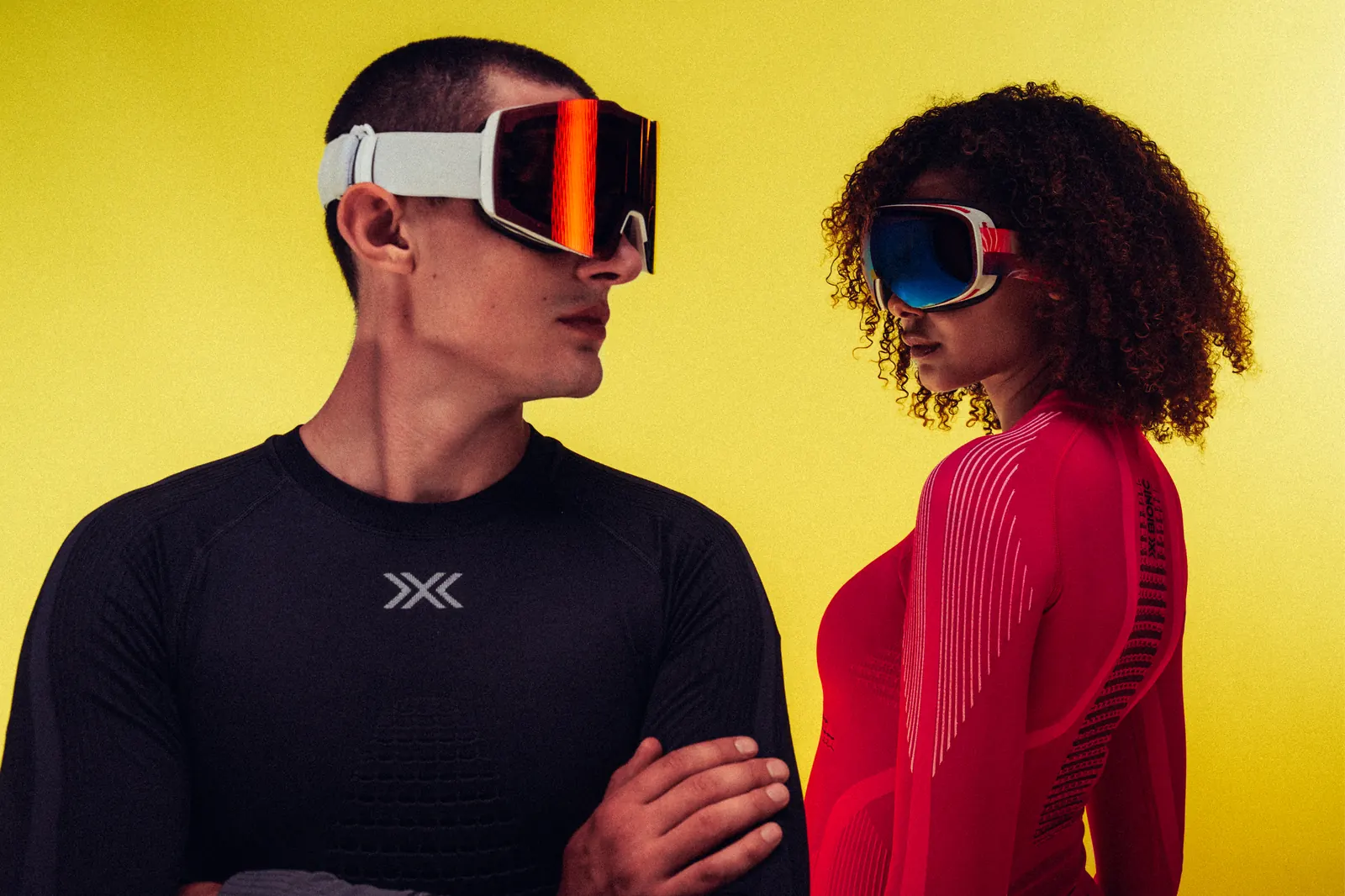Zwei Personen in X-Bionic Invent Funktionsshirts und Skibrillen vor gelbem Hintergrund