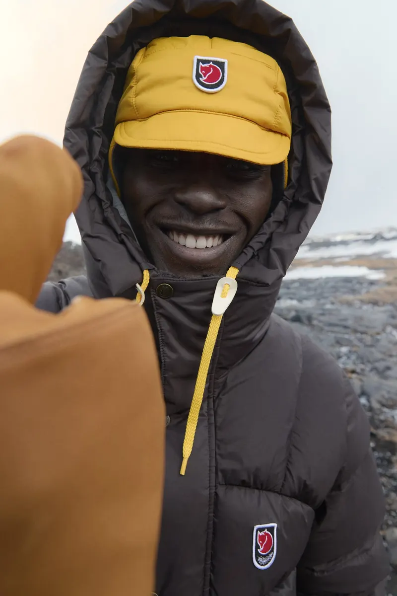 Laughing man in a dark brown Fjällräven down jacket with yellow beanie and hood