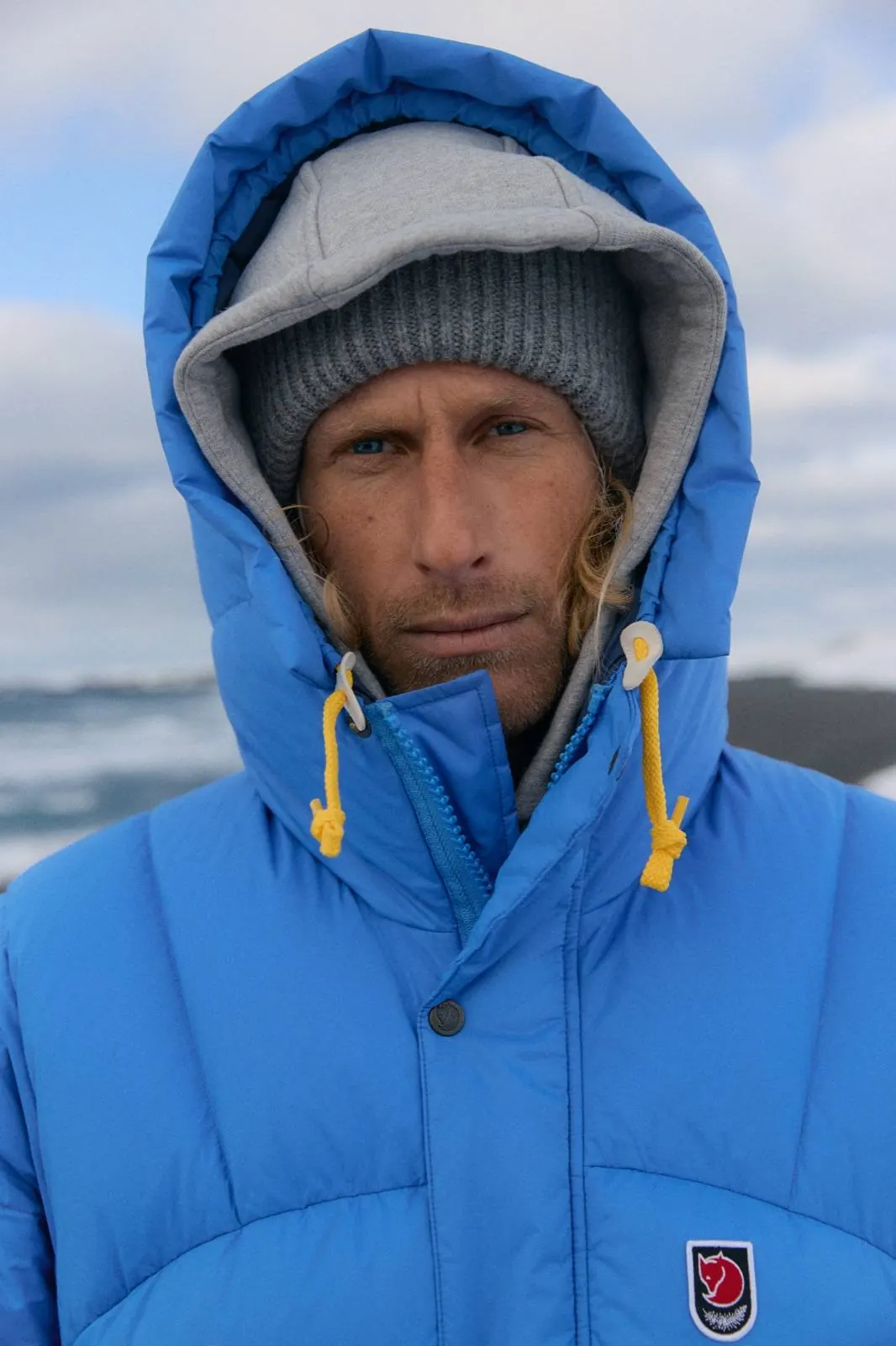 Mann in der blauen Fjällräven Expedition Down Jacket mit zugezogener Kapuze und gelben Kordeln