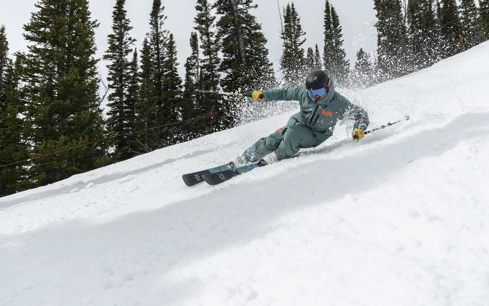 Skier in green Helly Hansen ski wear making a turn in the snow between pine trees